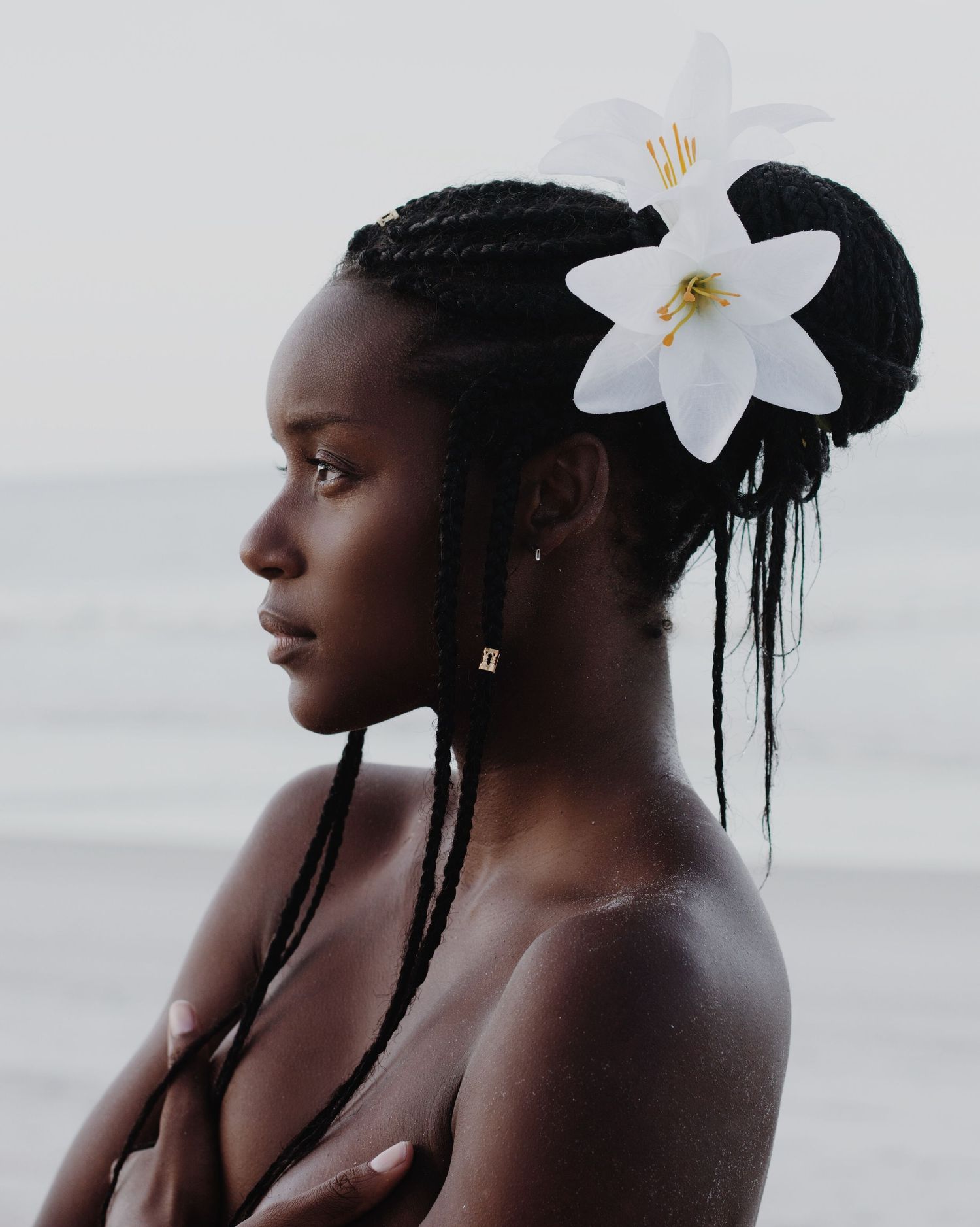 Minimalist beauty portrait featuring a white lily flower accent against dark braided hair.
