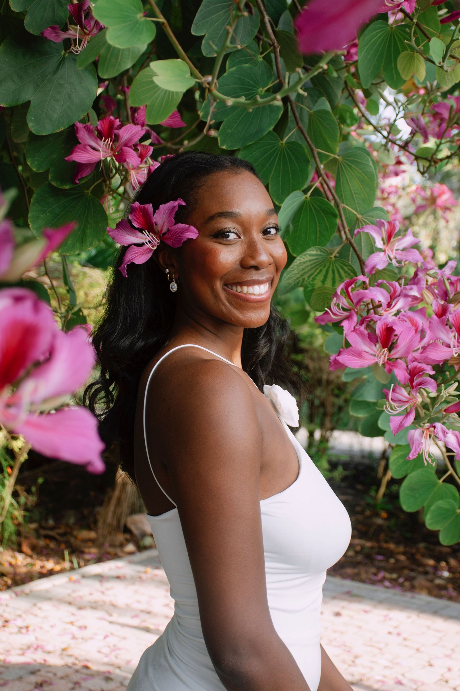 Portrait session under blooming pink orchid tree with white tank top.