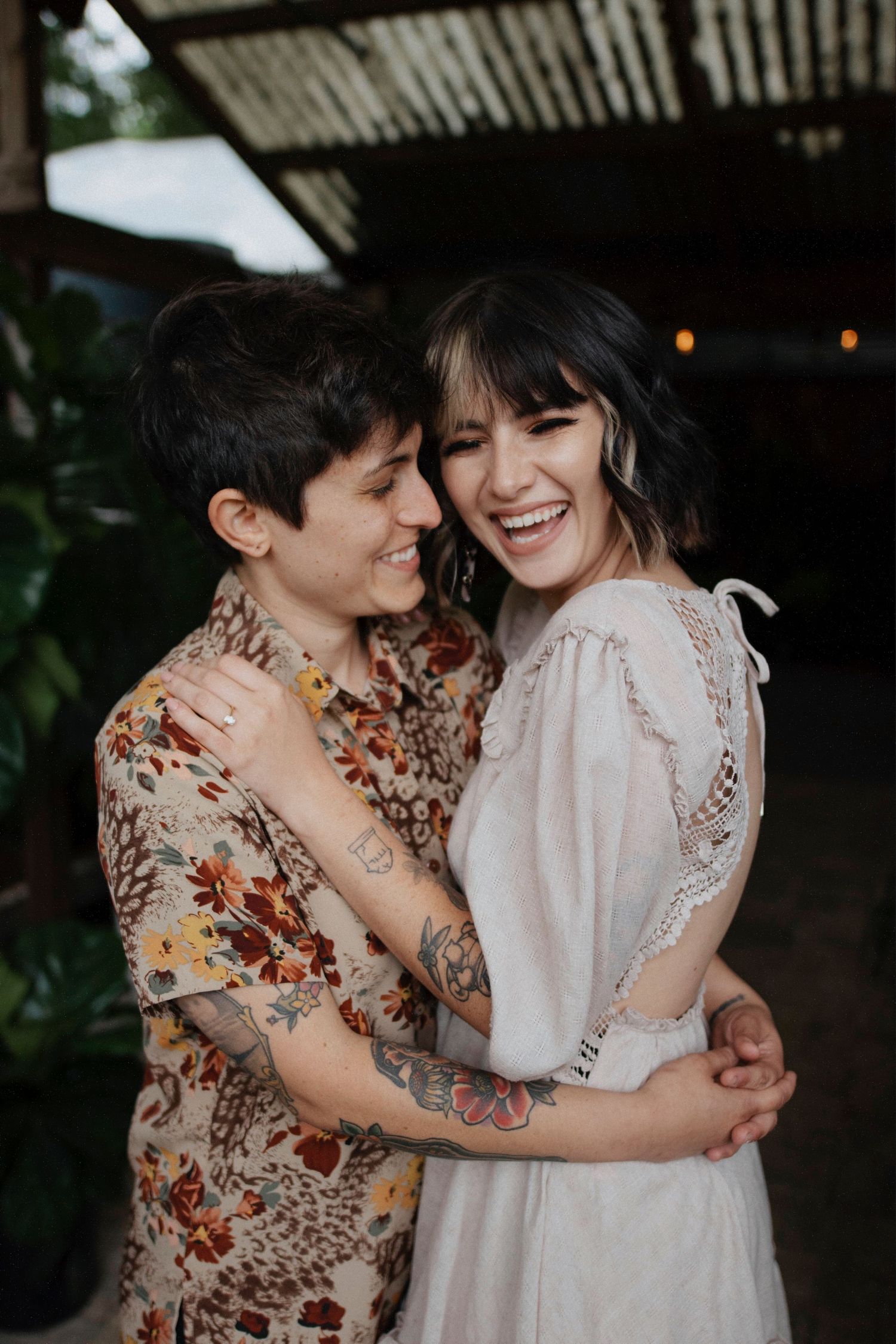 Two people share intimate moments and laughter while wearing floral and lace dresses in a romantic outdoor setting.
