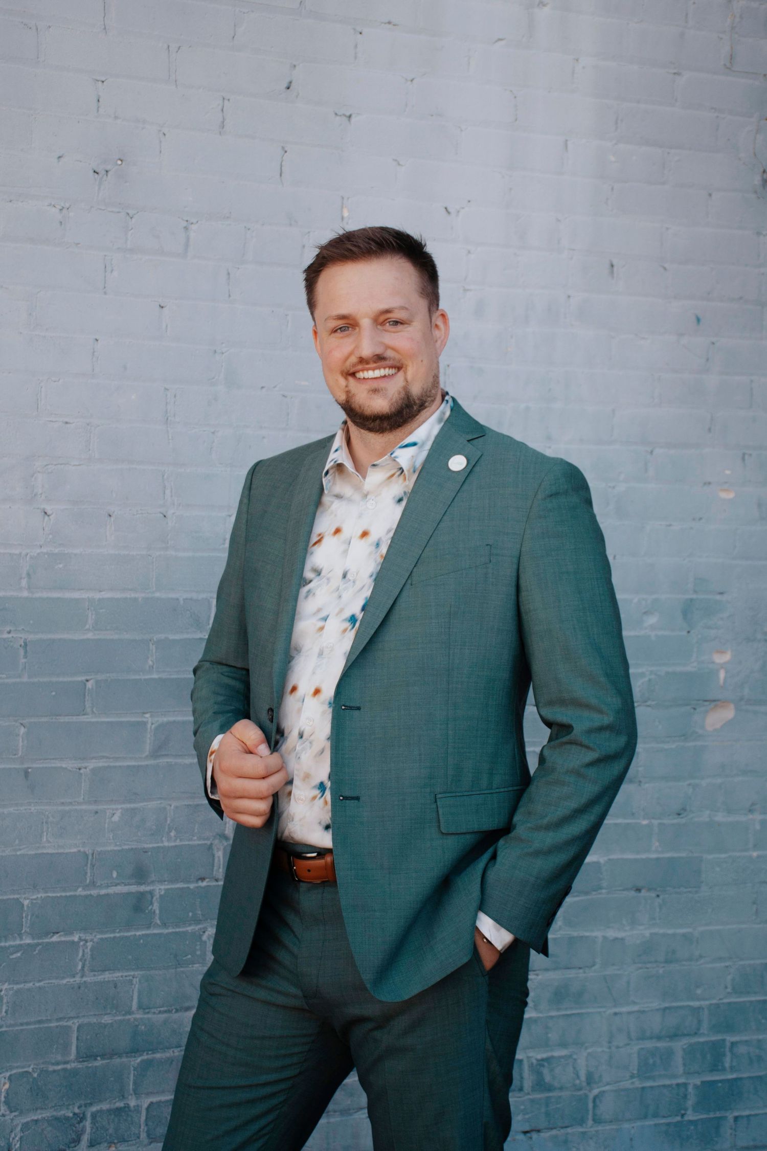 Business portrait series showing person in green suit against painted brick wall.