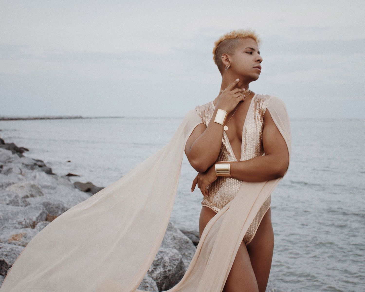 Ethereal beach photoshoot featuring flowing cream fabric against rocky coastal landscape.