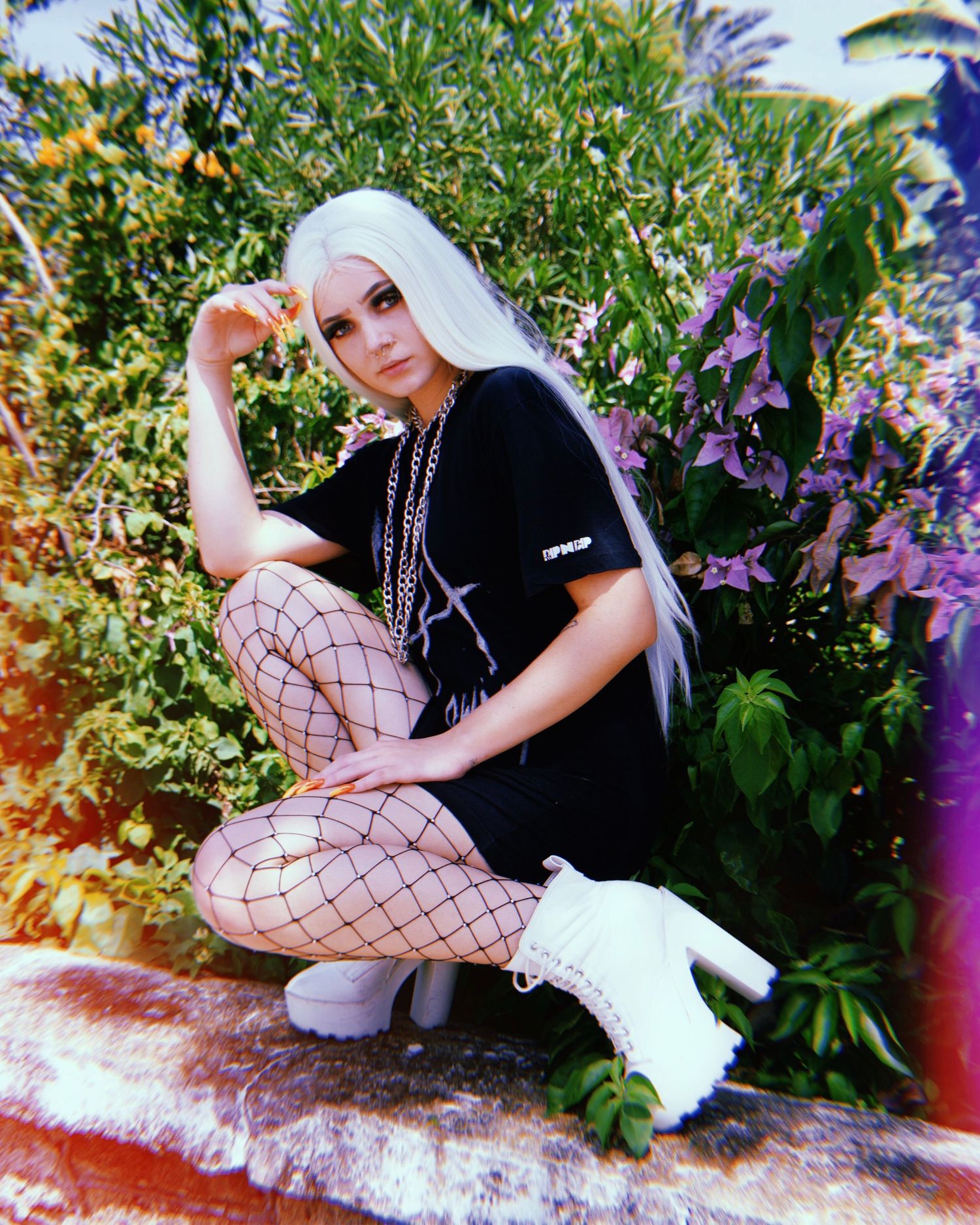 Artistic fashion poses near purple flowers and greenery in outdoor setting.