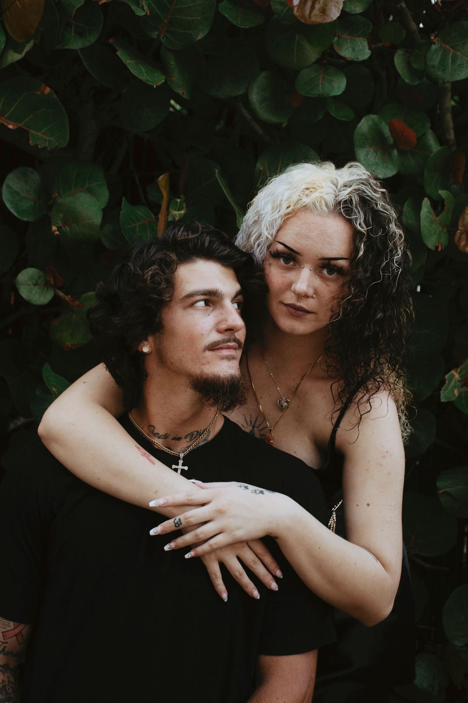 Intimate couple's maternity photoshoot against a backdrop of green leaves.