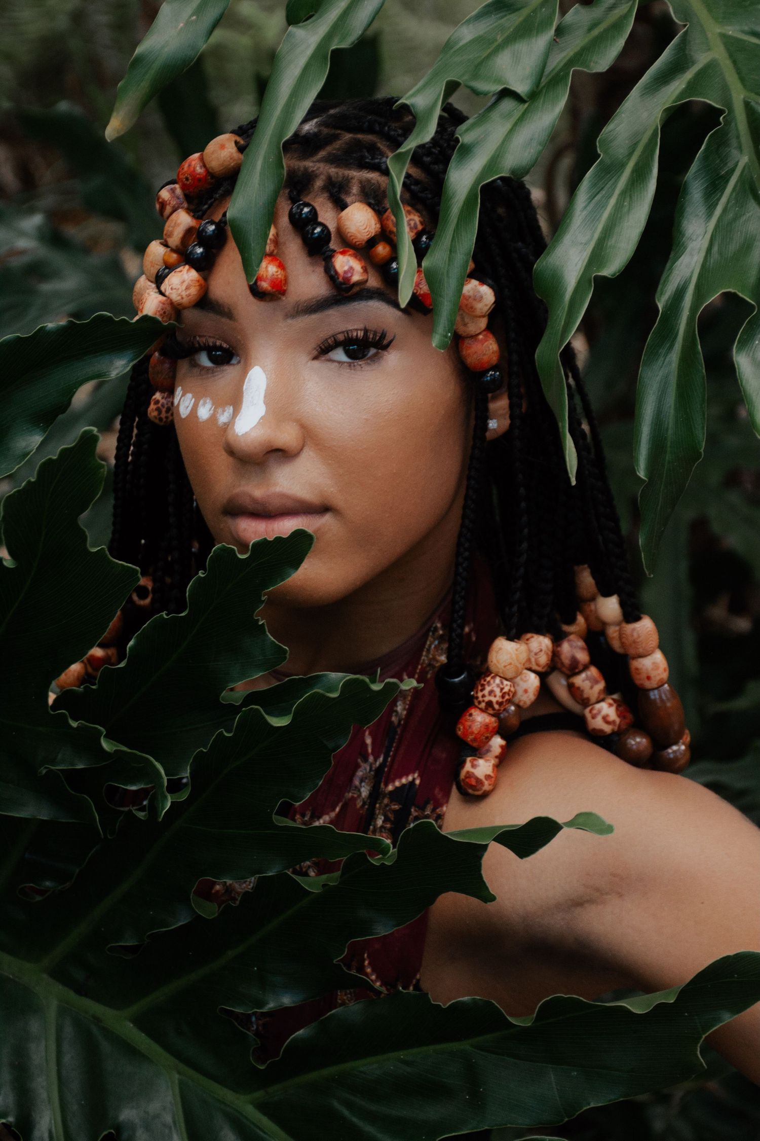 Artistic beauty portrait with foliage and wooden beads creating natural framing effect.