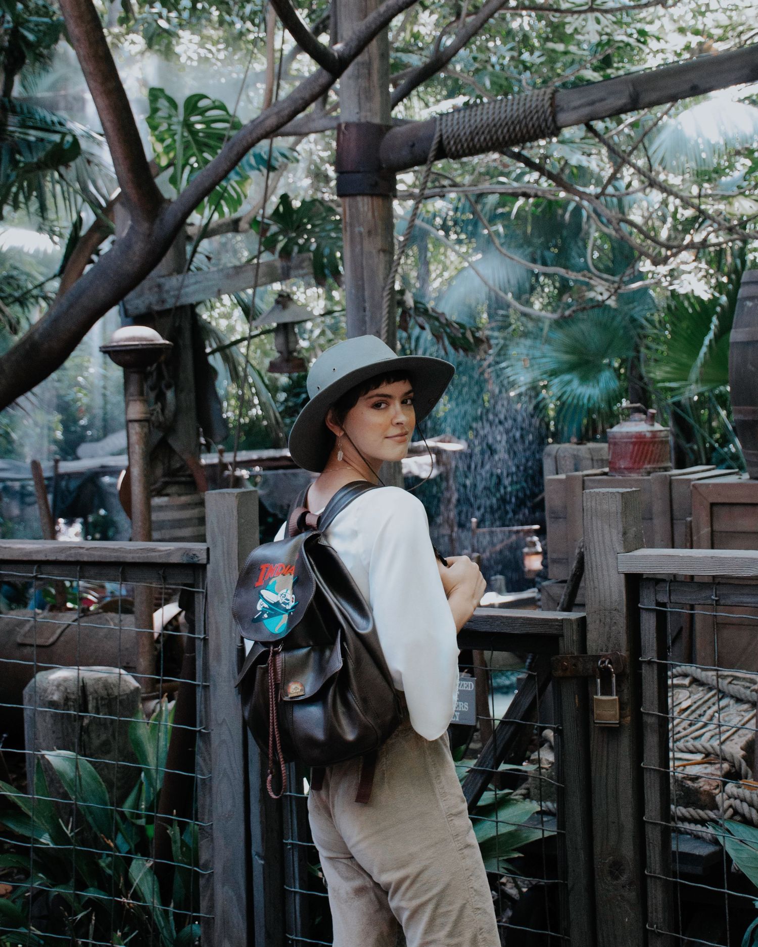 Cosplayer in vintage explorer outfit posing dramatically in lush garden setting.