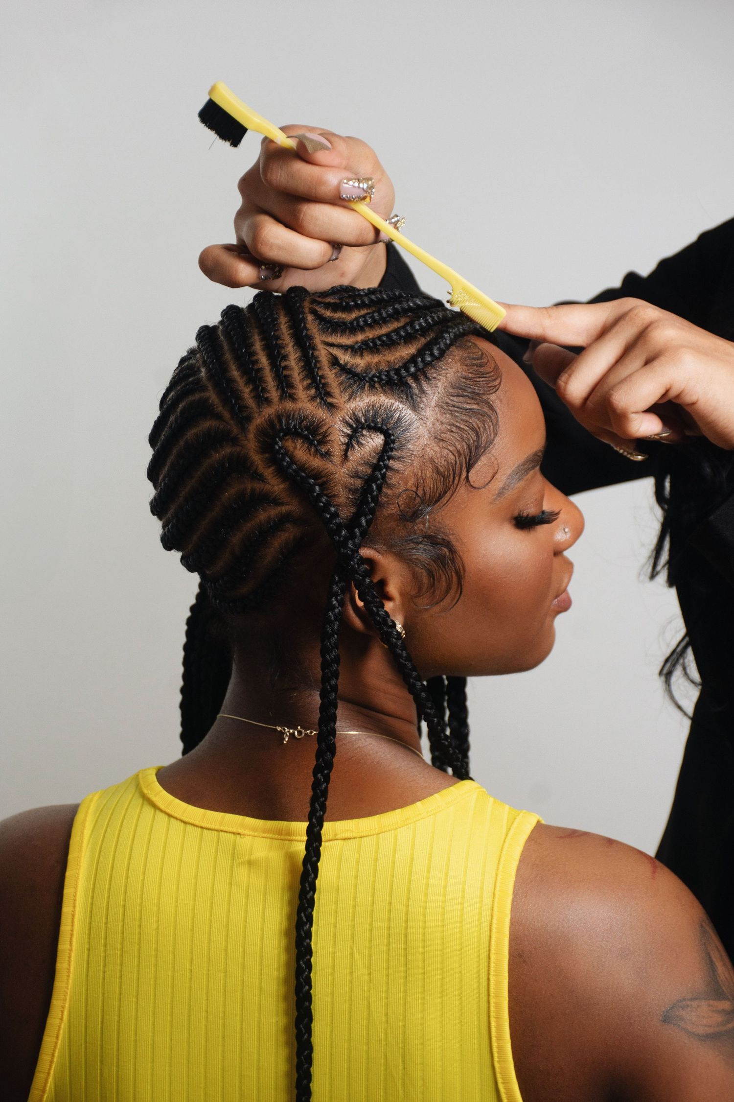 Close-up of detailed cornrow braiding technique being performed with yellow comb.