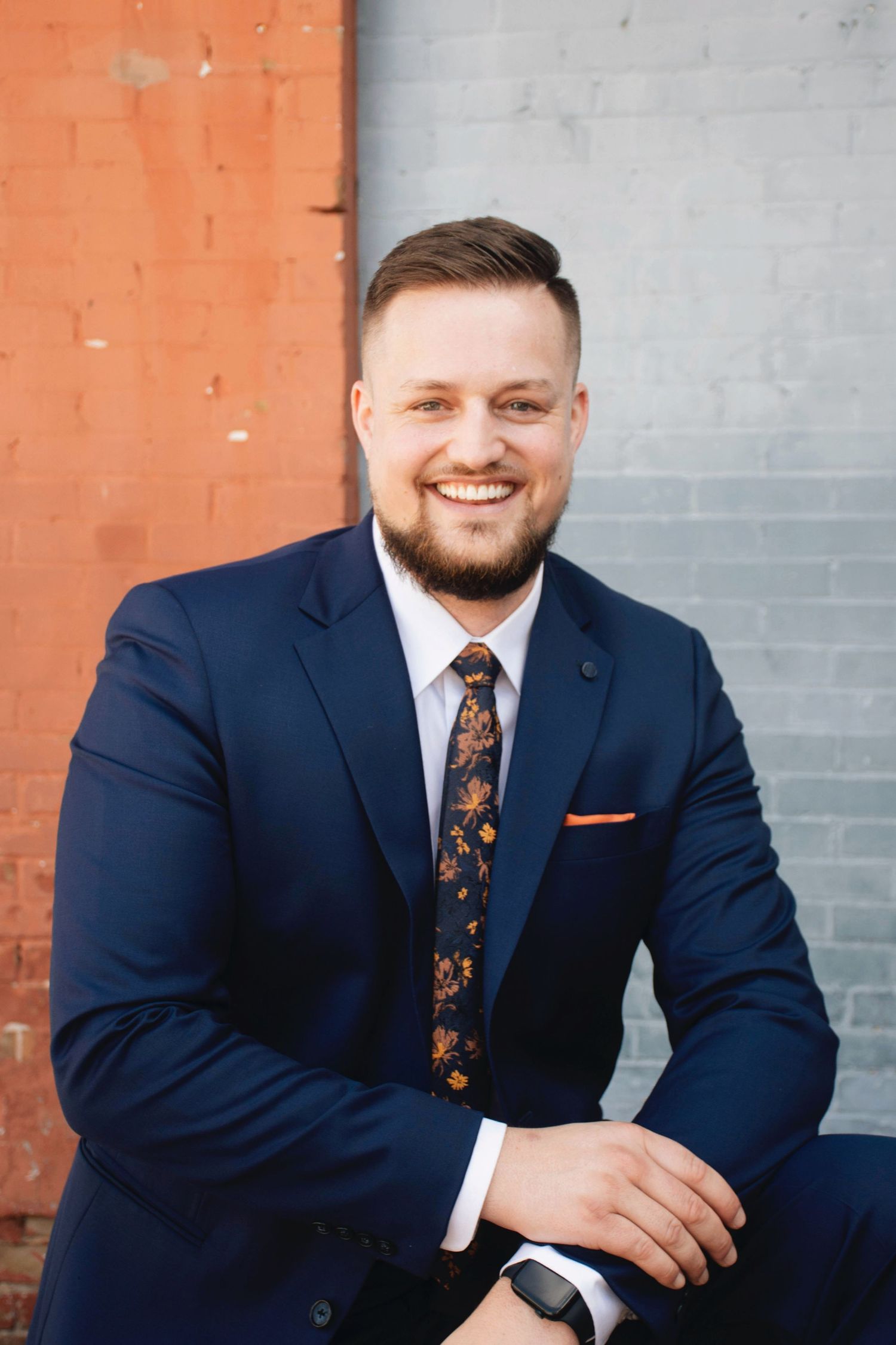 Business headshots in navy suit against mixed colored brick wall background.