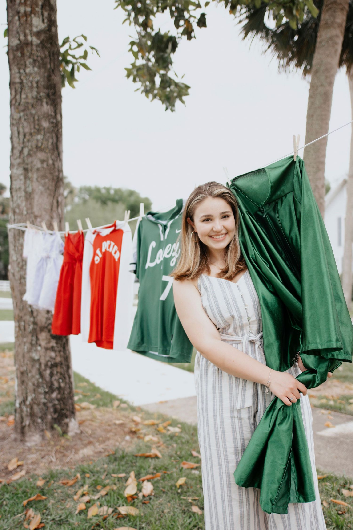 Green graduation gown and striped dress shown hanging on outdoor clothesline with red and white garments.