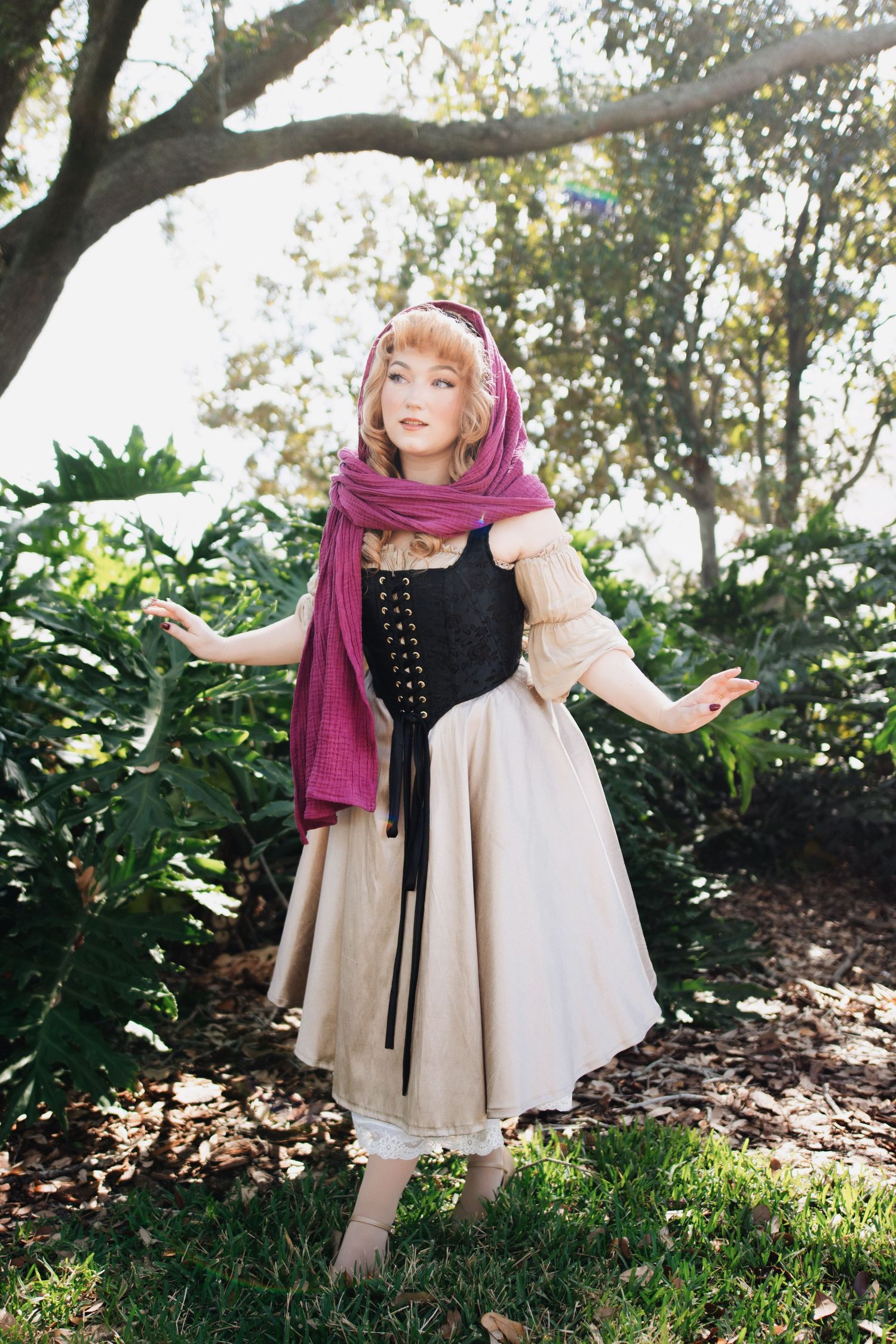 Playful outdoor portrait showing flowing beige dress and burgundy scarf in natural lighting.