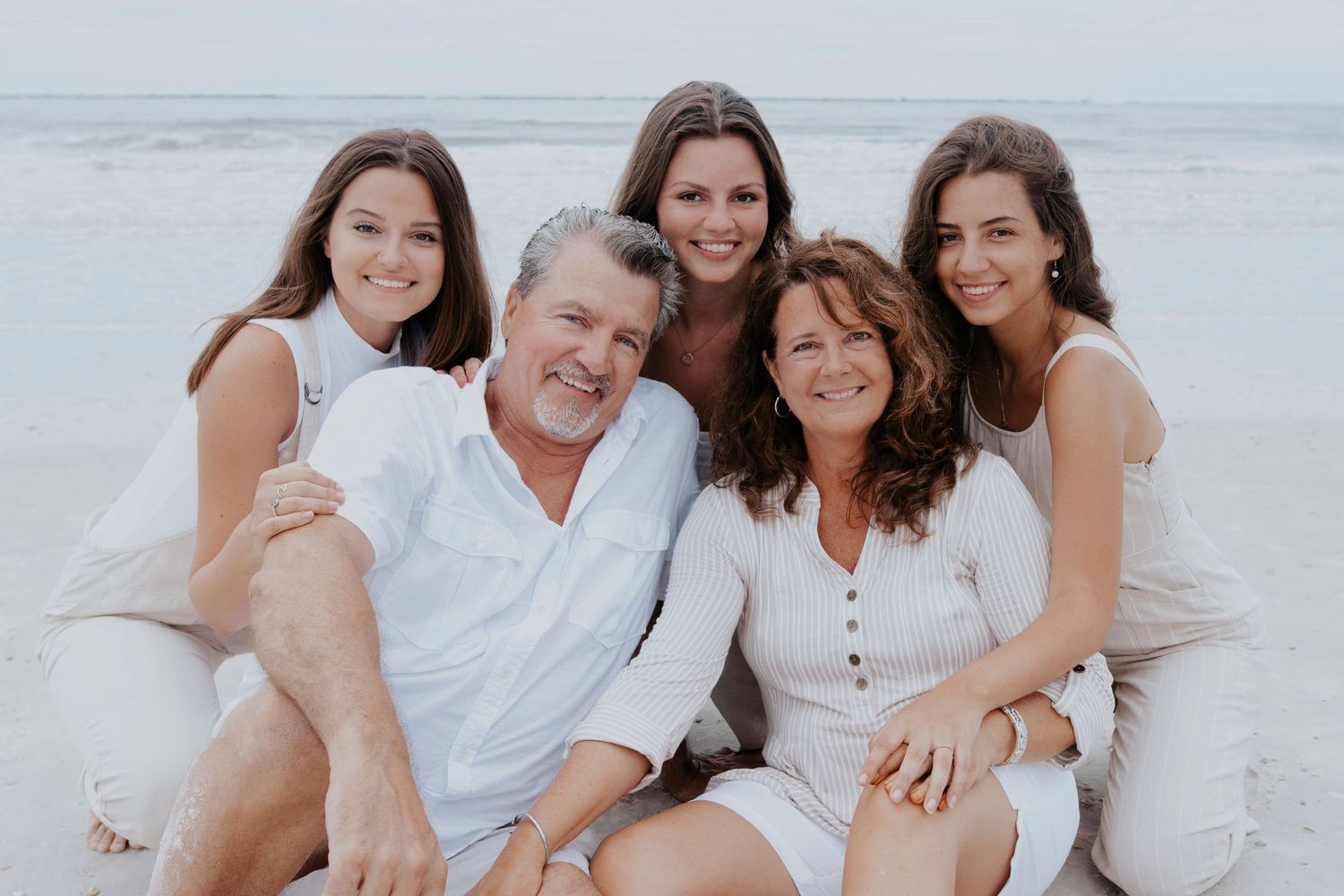A family wearing white clothing poses together on a sunny beach during a photo session.