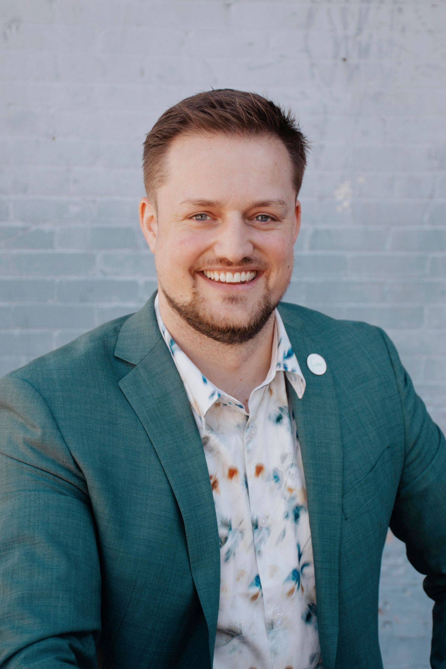 Professional headshots of person in green blazer and floral shirt against gray wall.