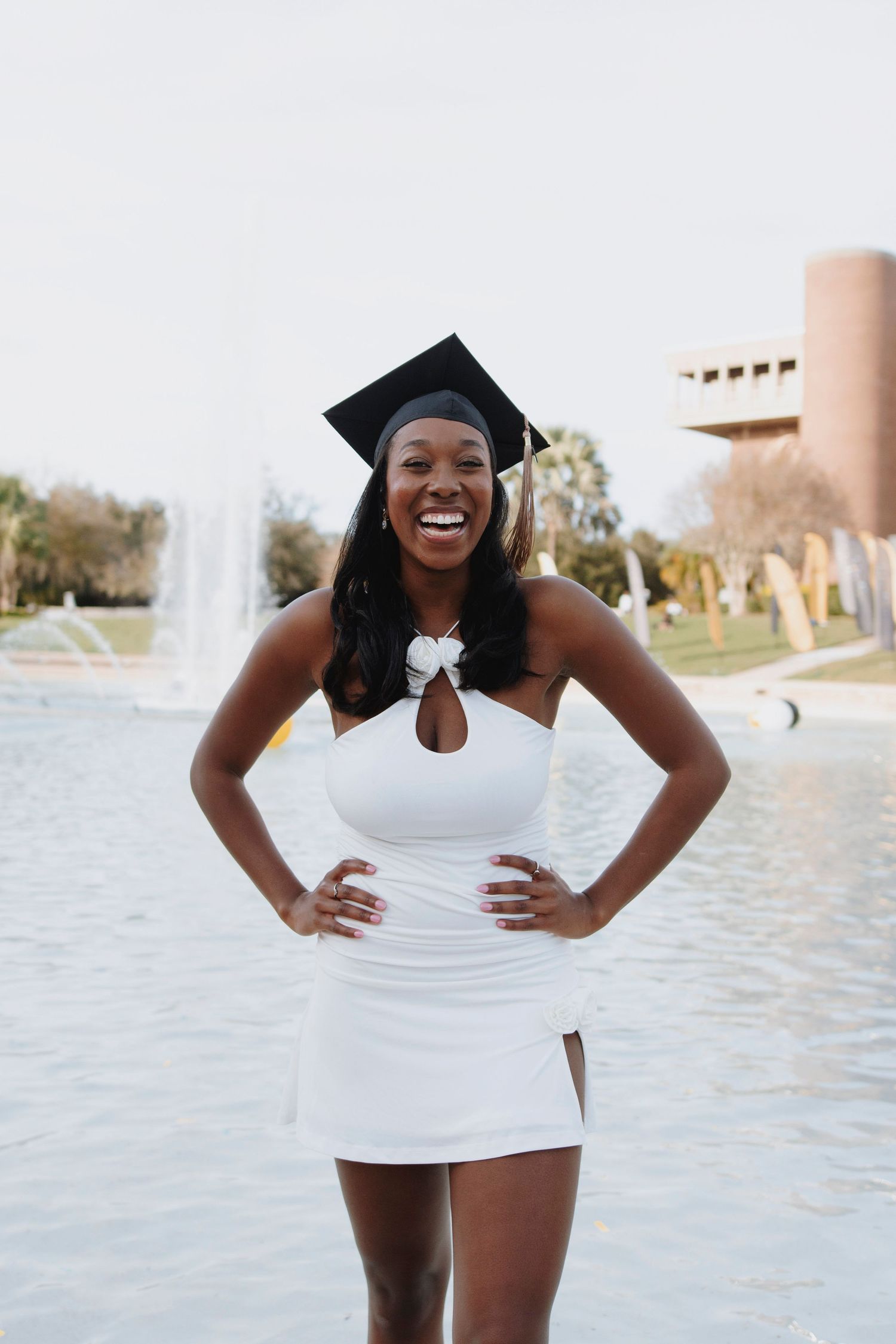 Joyful graduation celebration poses by waterfront in white dress.