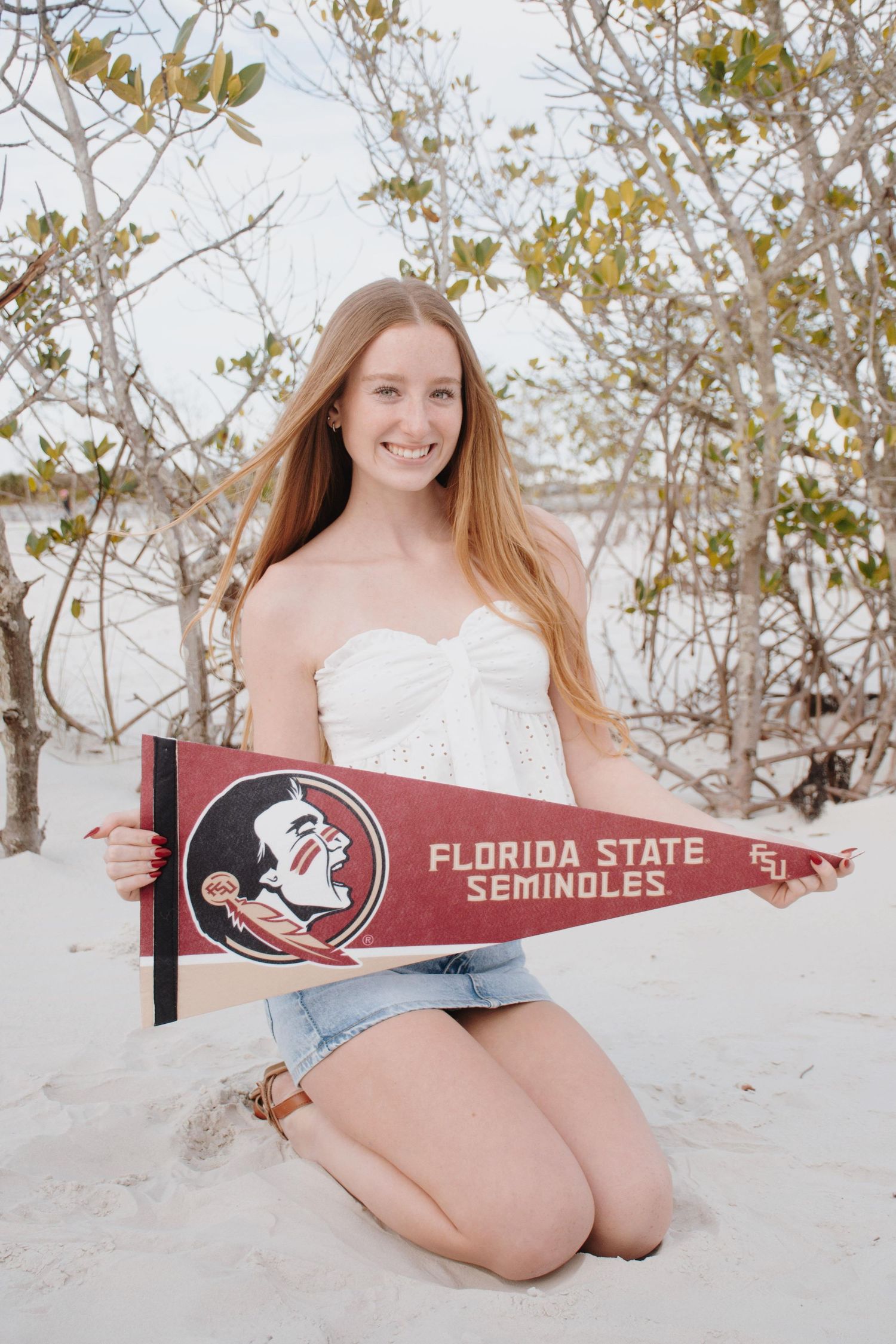 Young woman holds Florida State Seminoles pennant while sitting on white sandy beach.