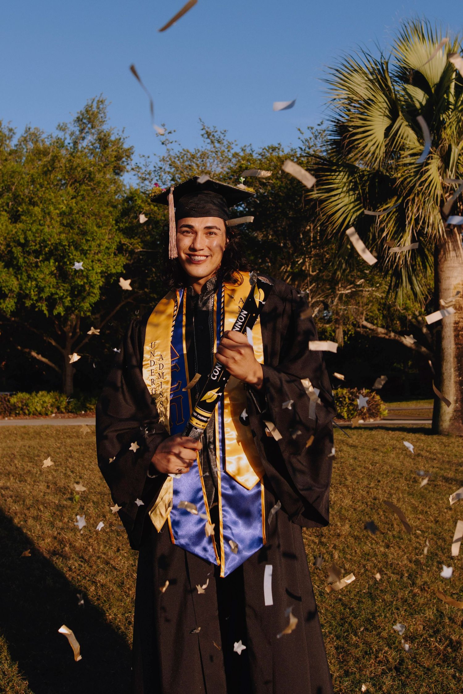Graduate celebrates with confetti toss during outdoor graduation photoshoot.