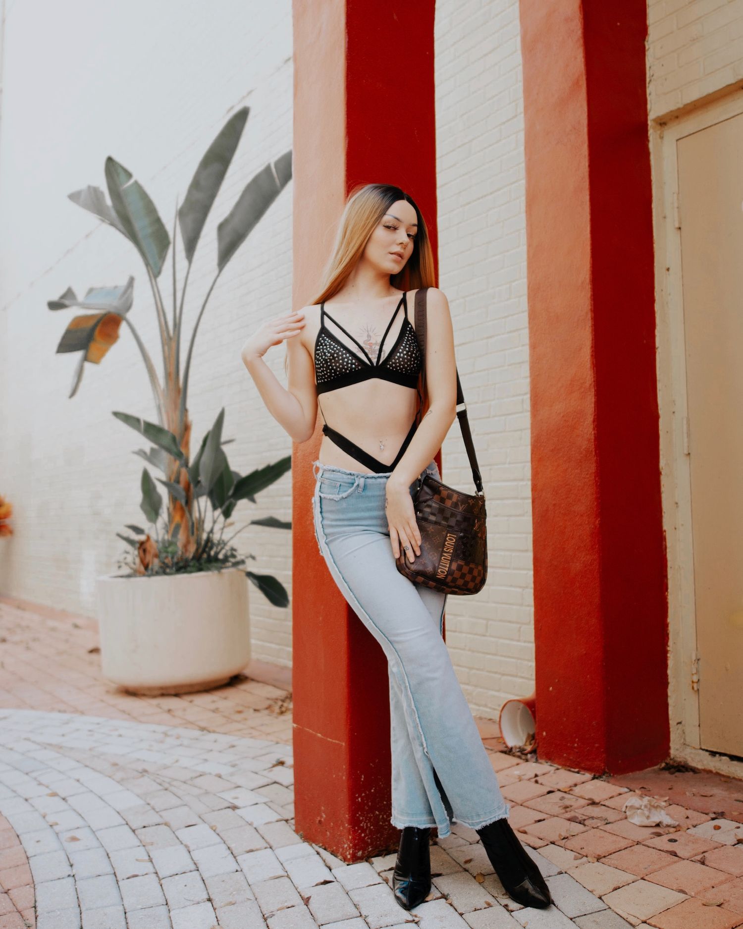 Fashion model in blue dress and black accessories poses against white and red pillars.