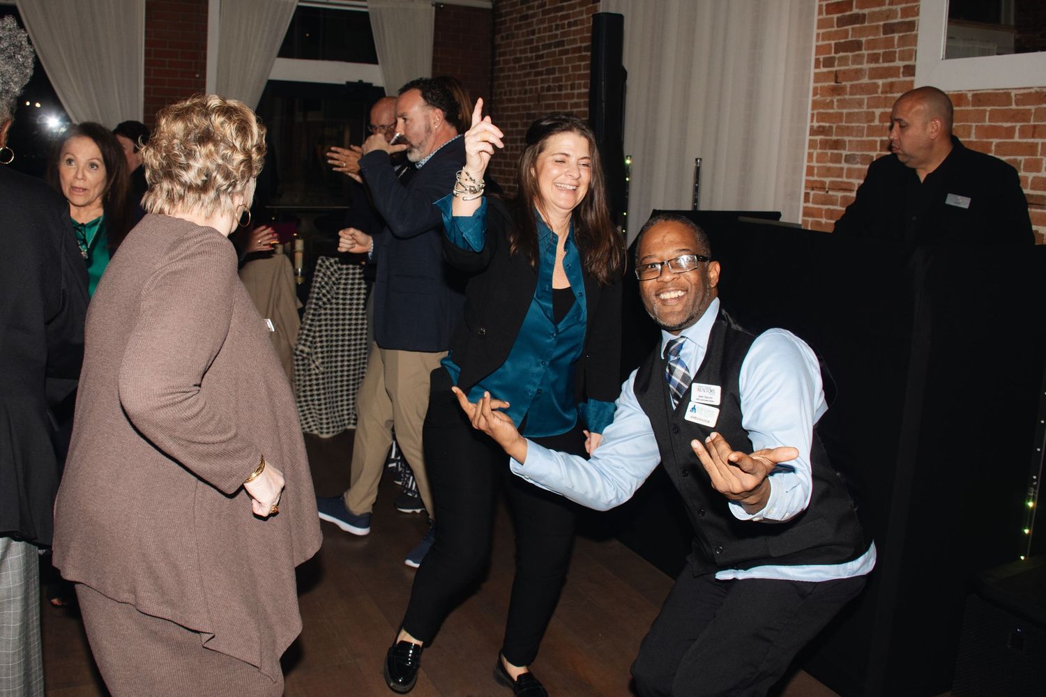 People dancing and having fun at what appears to be a party or social gathering in an indoor venue with brick walls.