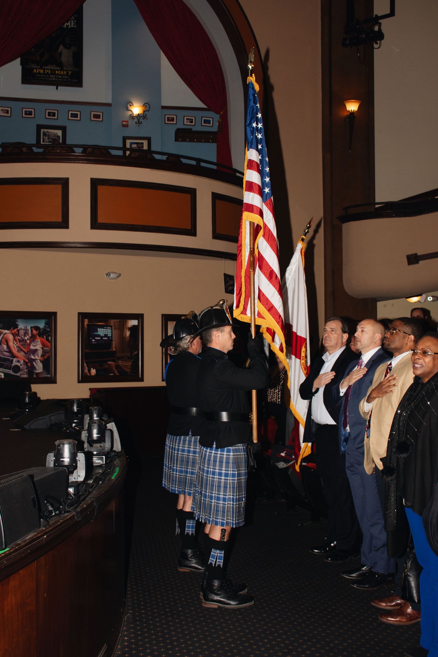 A group of people stand at attention during a patriotic ceremony with American flags displayed in an indoor venue.