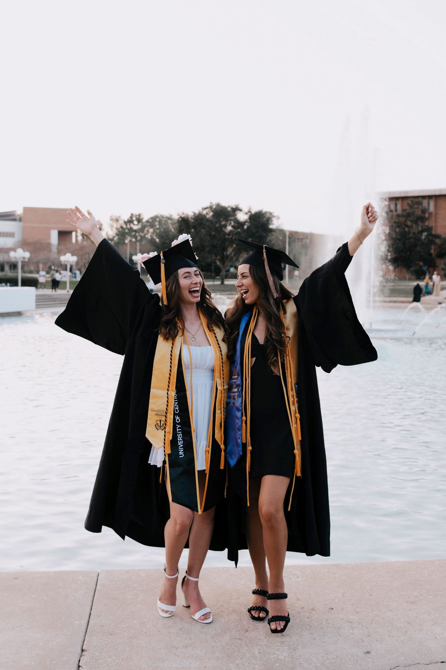 Graduates in black robes and gold stoles walking together near a reflective pool.
