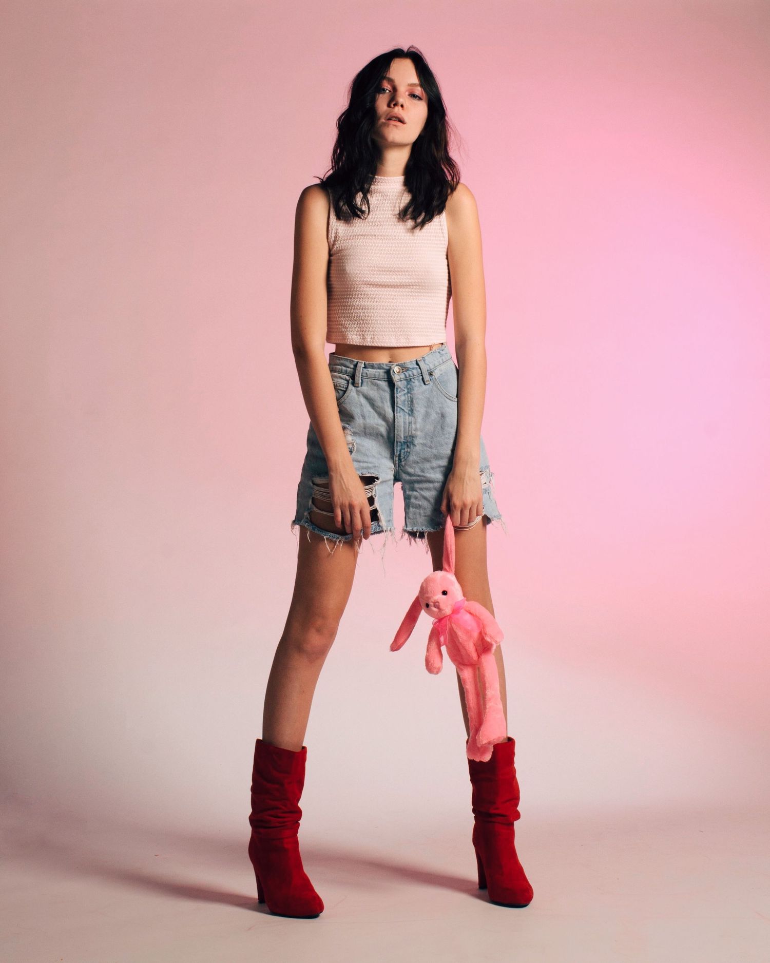 Fashion shoot against pink backdrop featuring crop top, denim, and red boots.