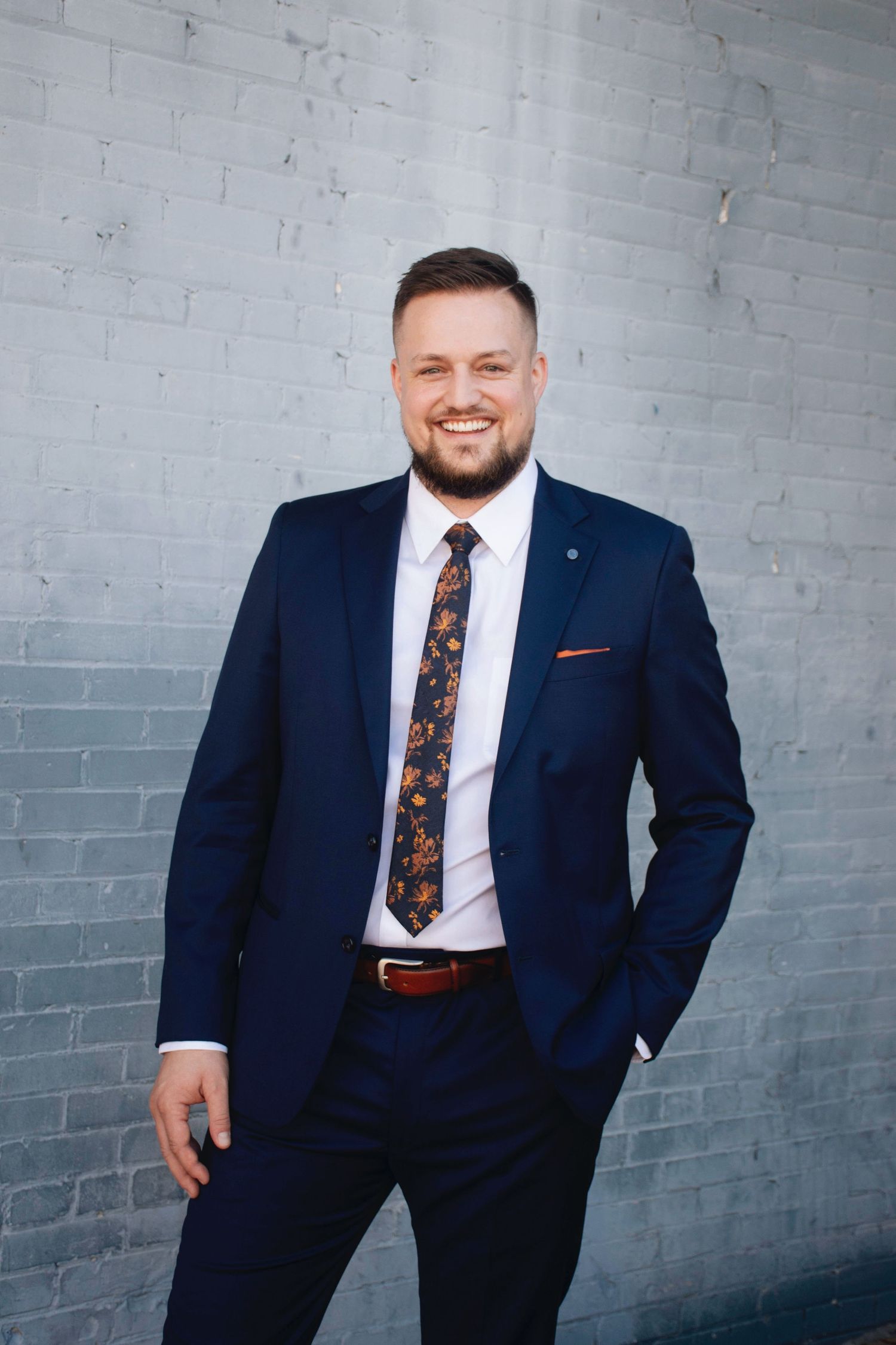 Professional portraits in navy suit against industrial gray wall background.