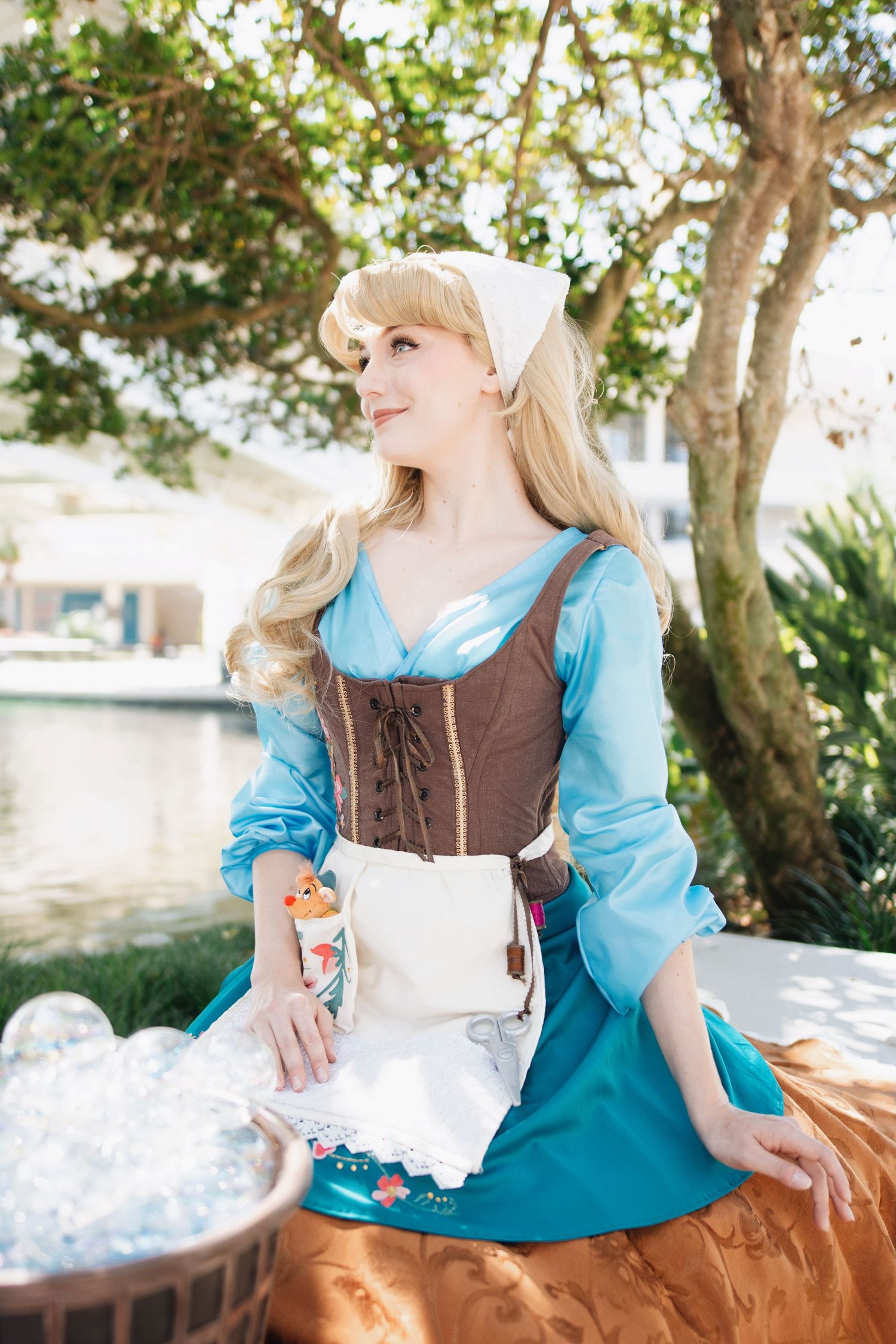 A costumed performer in blue and brown dress sits gracefully beside a basket outdoors.