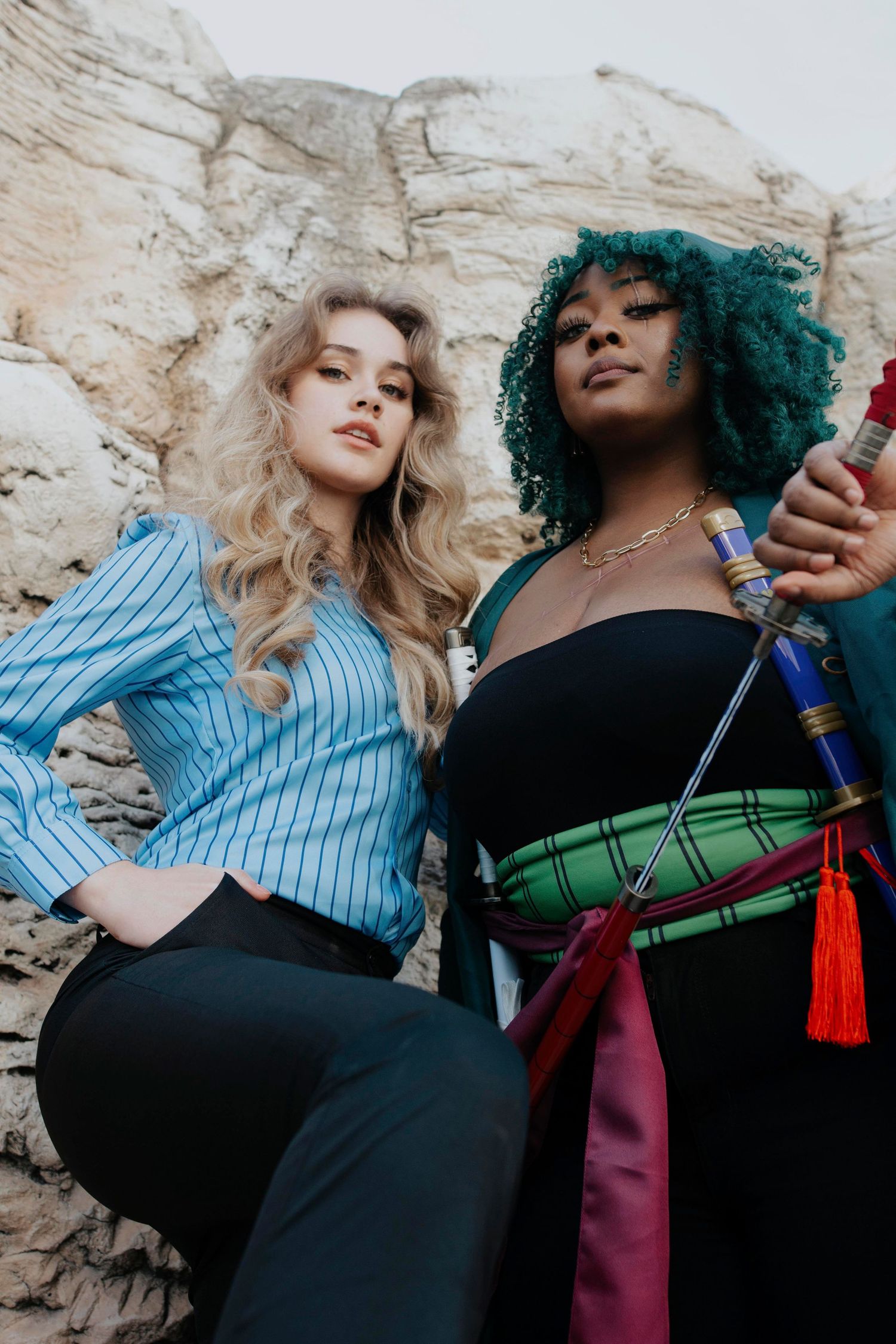 Two models in stylish outfits pose dramatically against a rock wall.