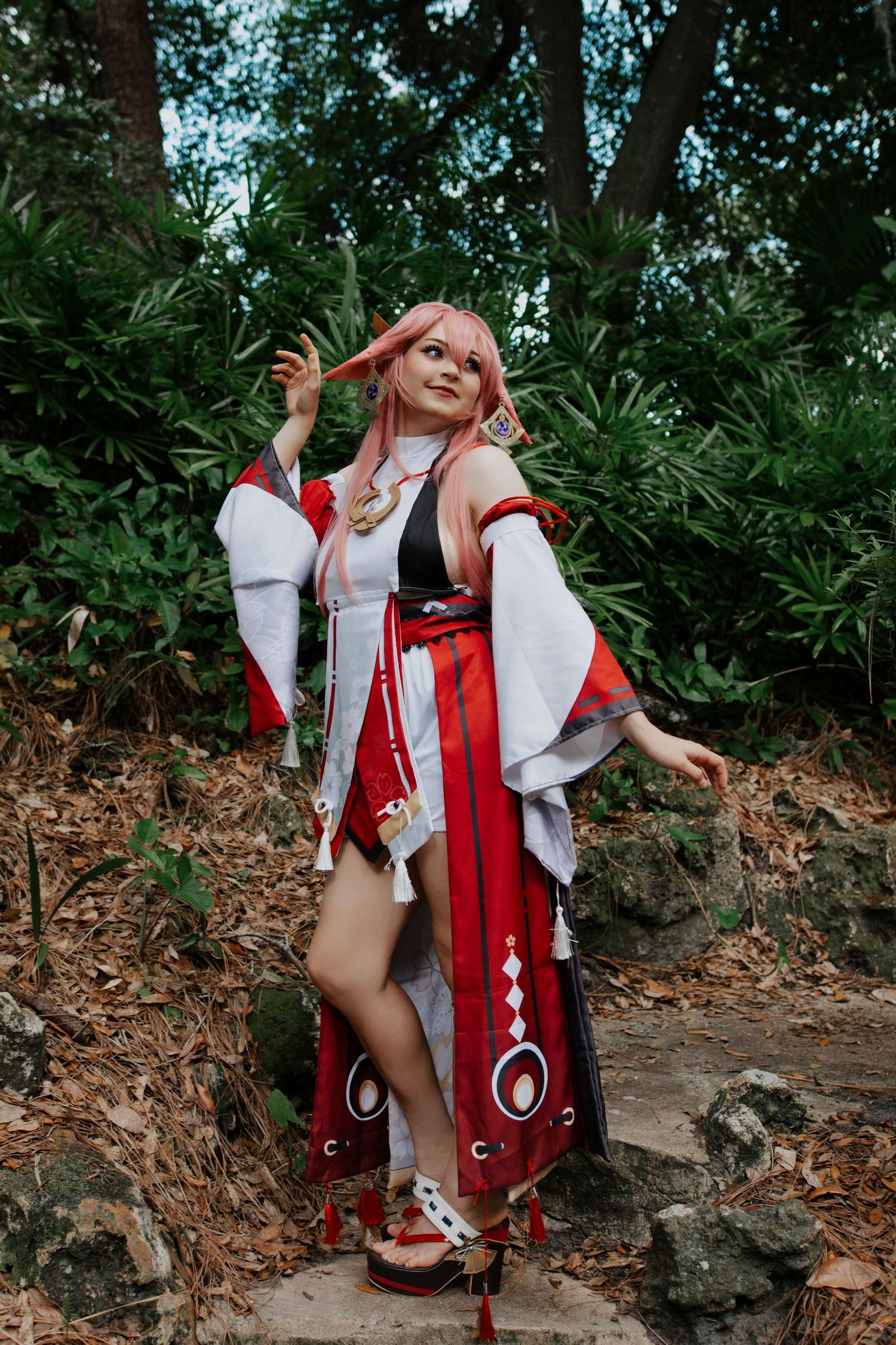 Outdoor cosplay photography featuring red and white traditional-style costume among trees.