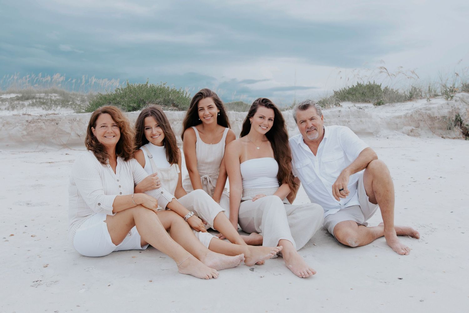 Group portrait of family members relaxing together on white sand beach.
