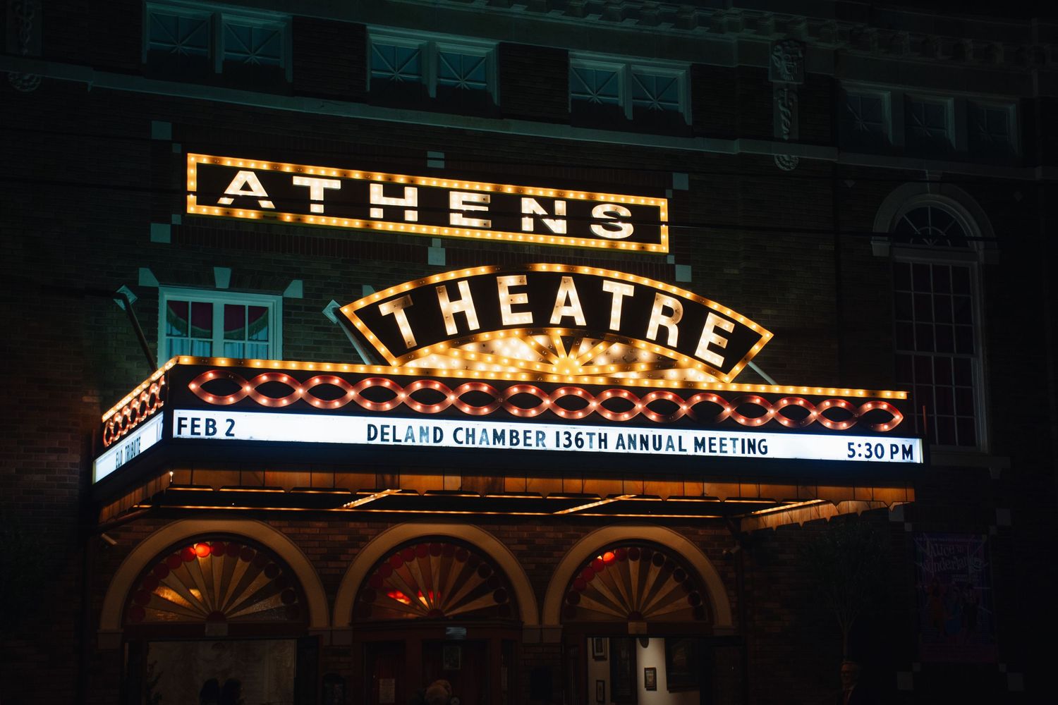 Vintage illuminated theater marquee signs glowing at night in a row along a city street.