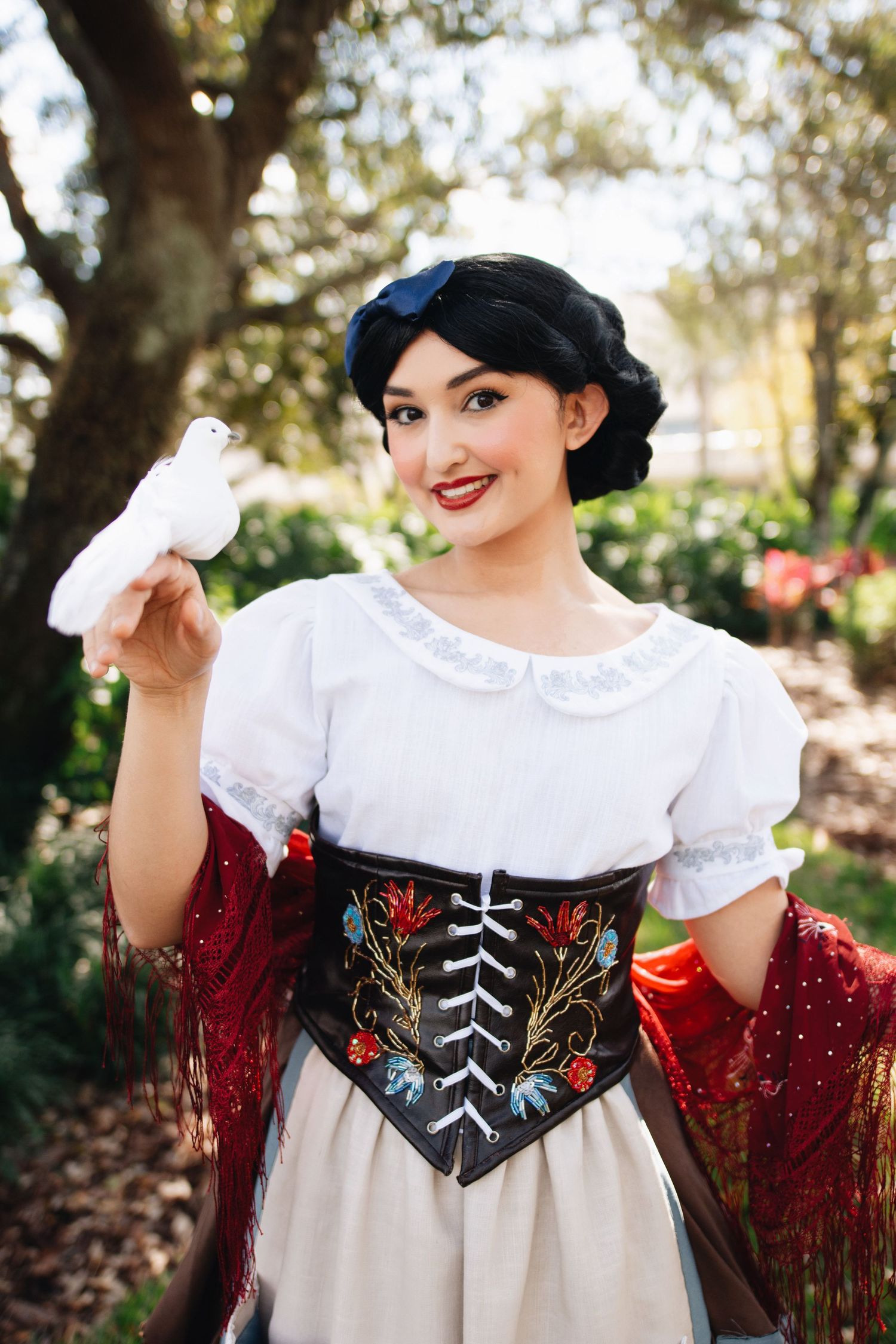 A cosplayer in a traditional peasant costume featuring a white blouse, embroidered corset and red shawl.