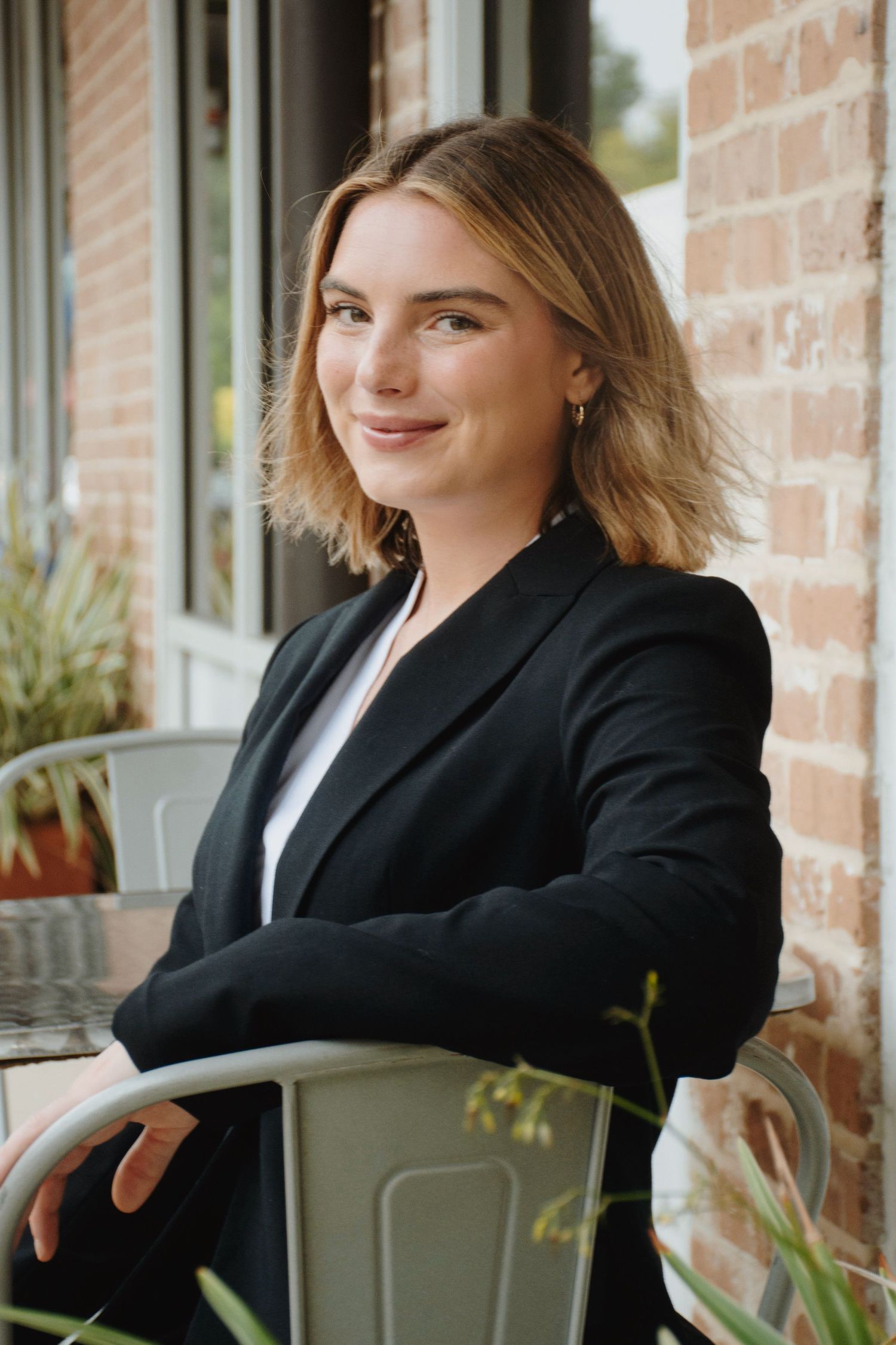 Casual business portrait seated outdoors by brick wall.