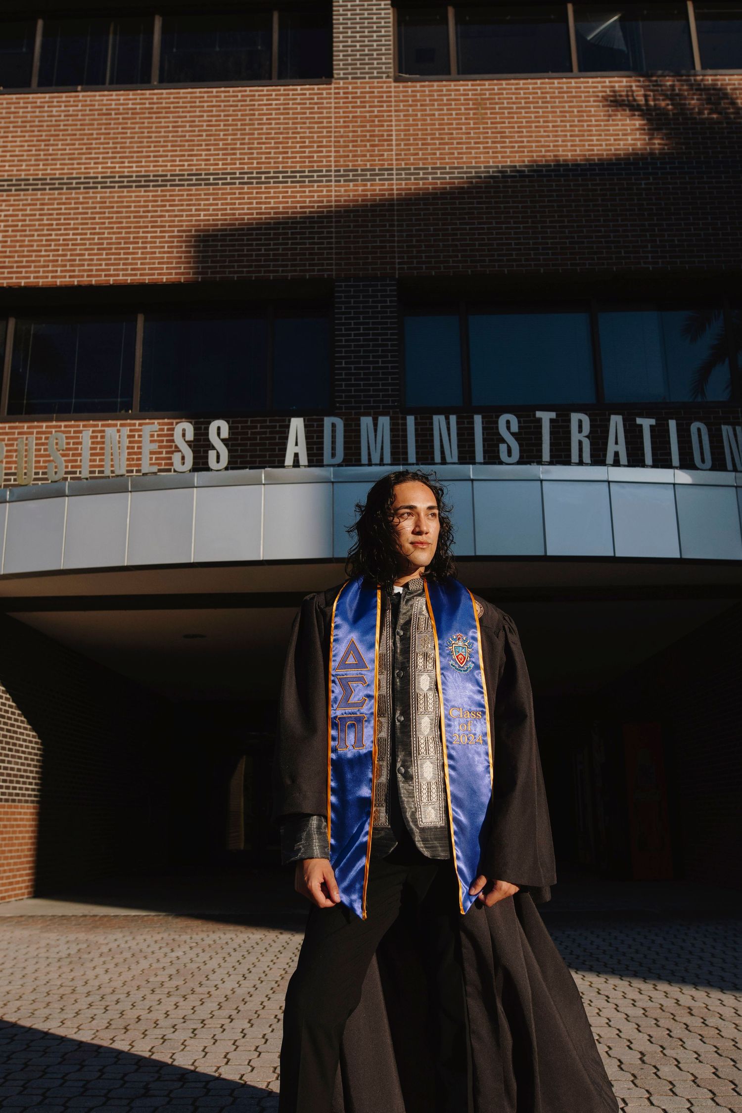 Graduate poses in front of Business Administration building wearing academic regalia.