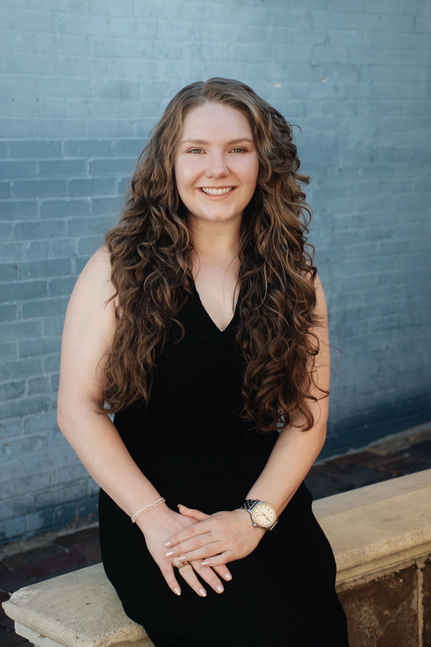 Professional headshots featuring warm smiles and long curly dark hair against an industrial backdrop.