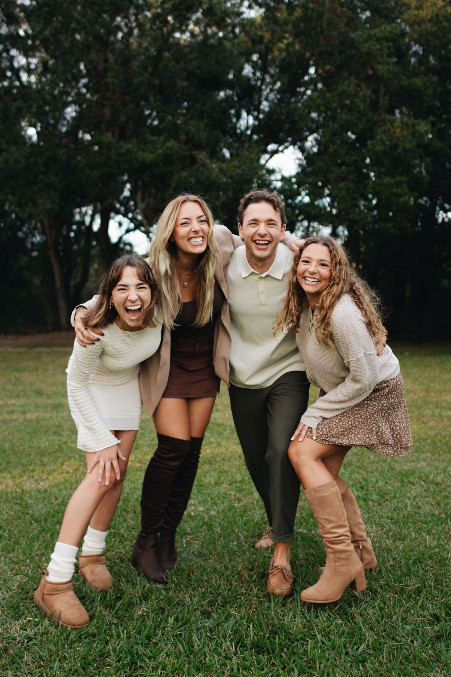 A group of friends laughing and posing together on grass in coordinated neutral-toned casual outfits.
