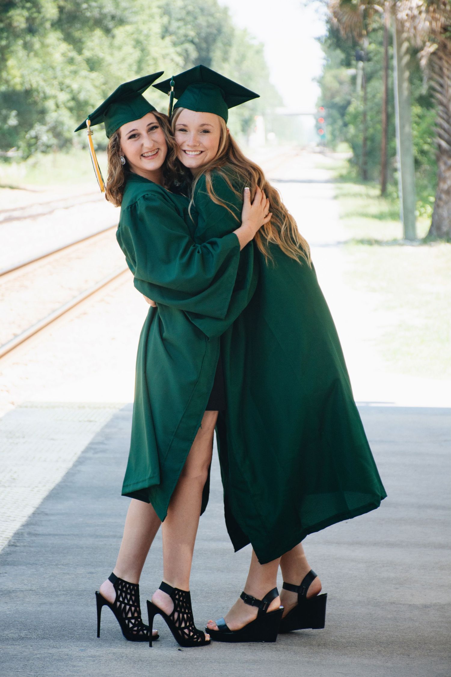 Two graduates in emerald green caps and gowns show off their stylish black heels during a celebratory photoshoot.