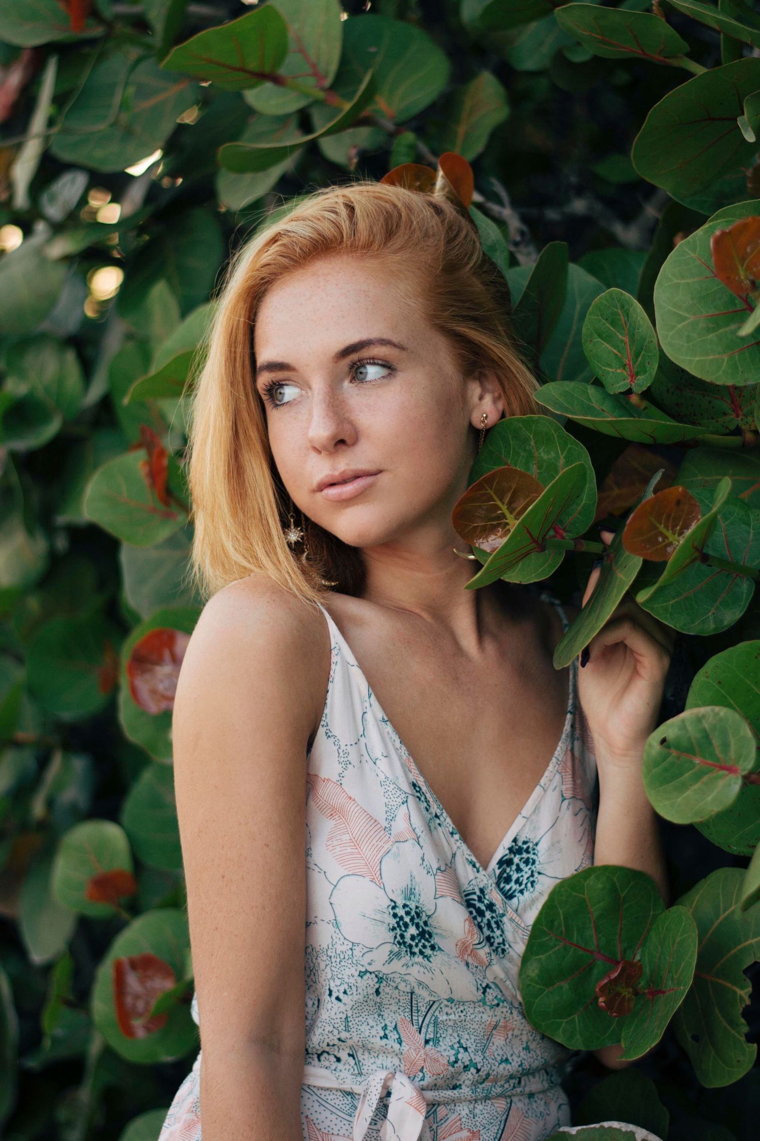 Floral dress portrait session among lush green foliage and leaves.