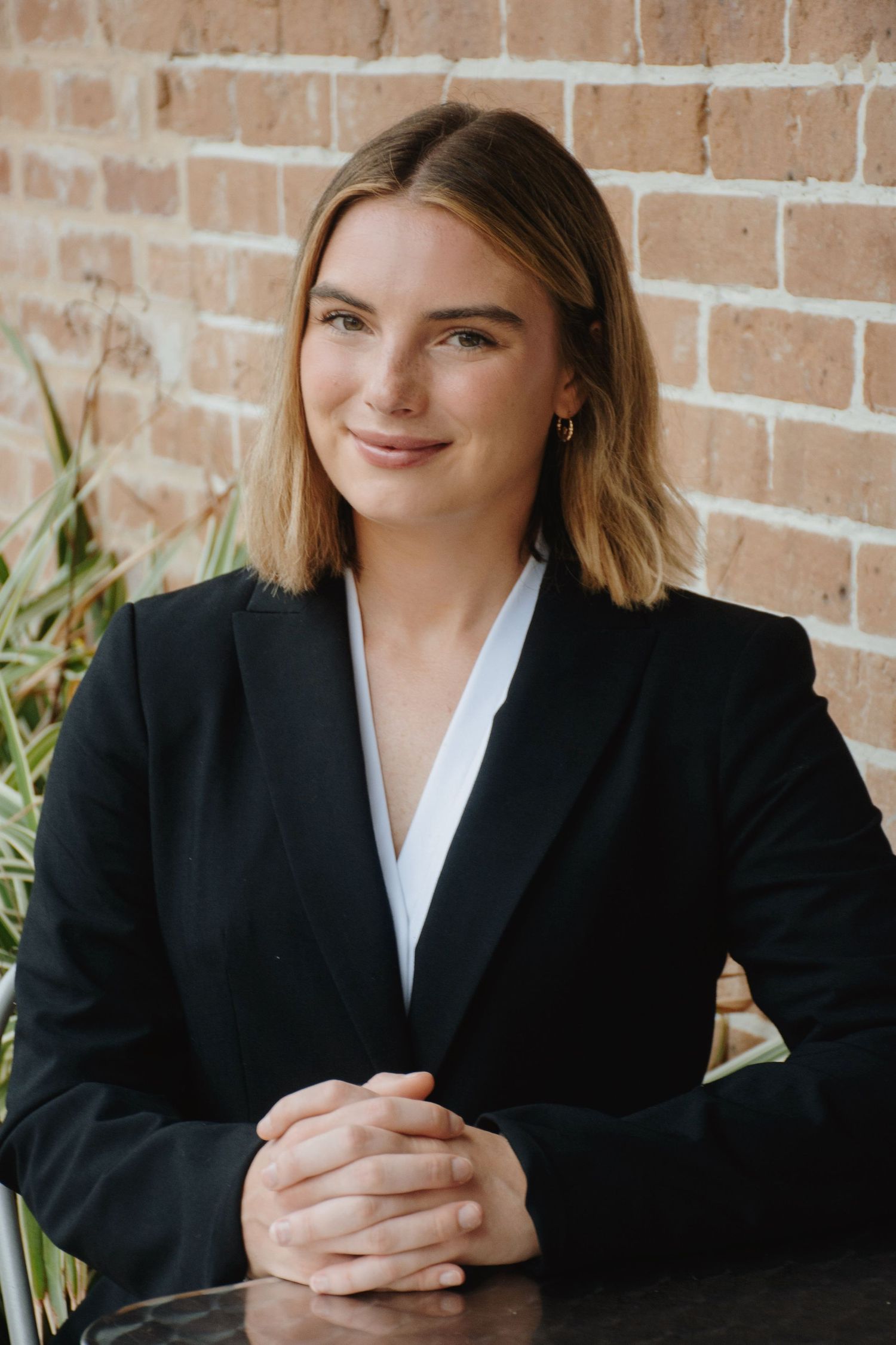 Professional seated portrait in business attire with clasped hands.