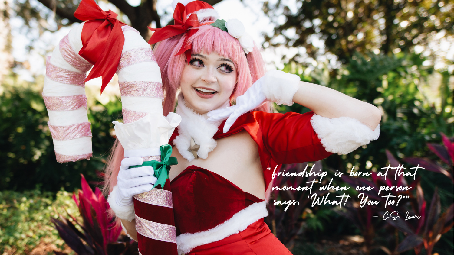 A cosplayer in a red and white holiday-themed costume poses cheerfully in an outdoor garden setting.