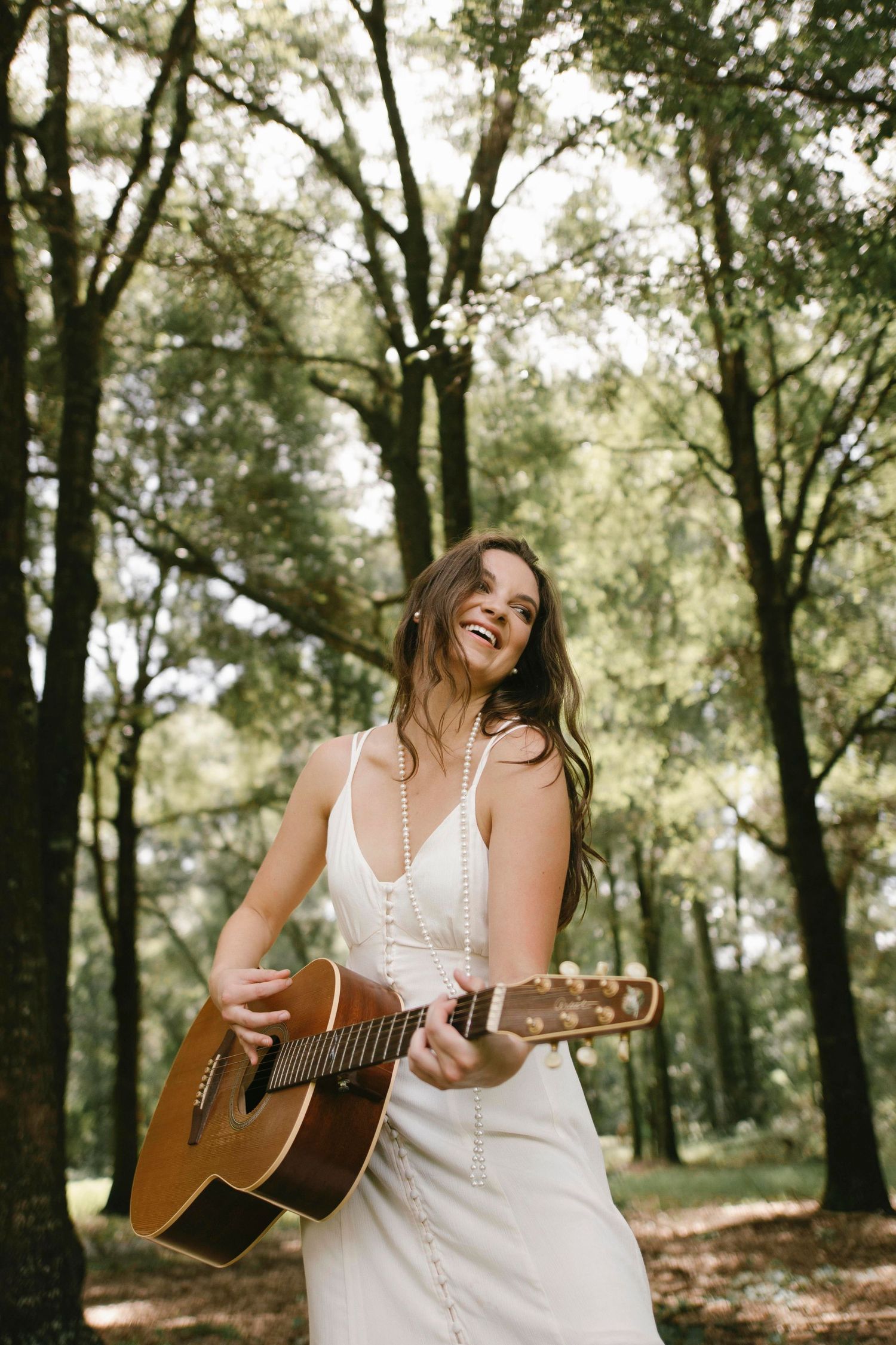 Natural light portrait session in forest setting with acoustic guitar and white dress.