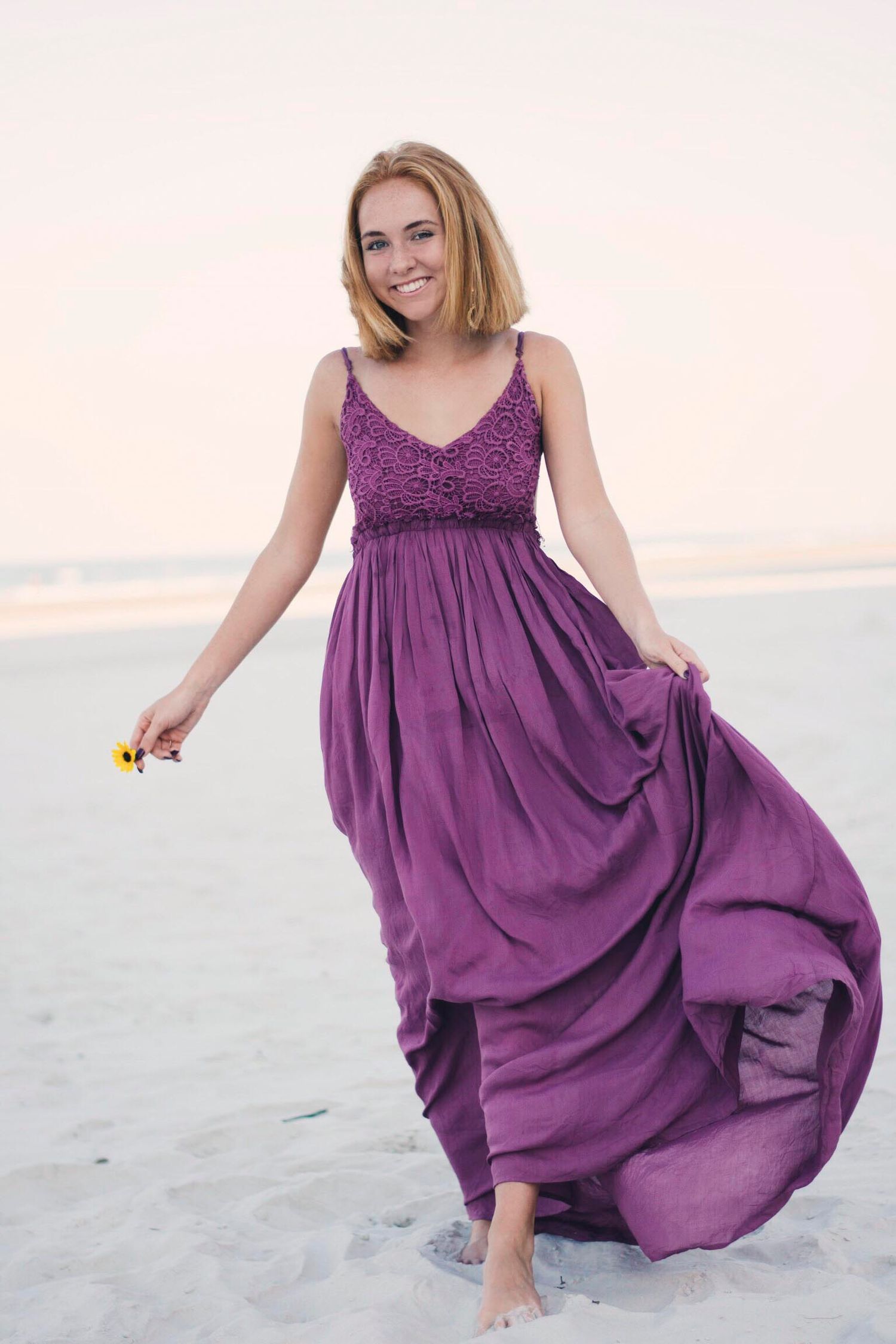 Purple flowy dress twirls on sandy beach during sunset photoshoot.