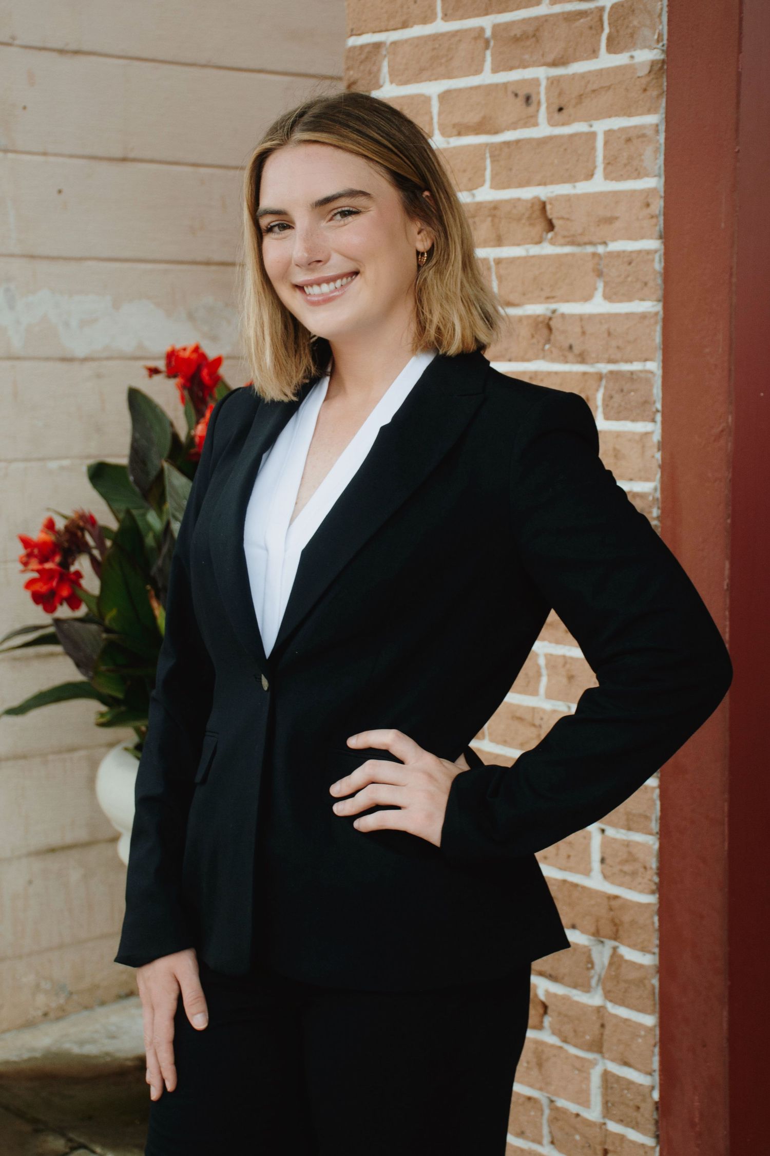 Business portrait in black blazer with confident pose against brick background.