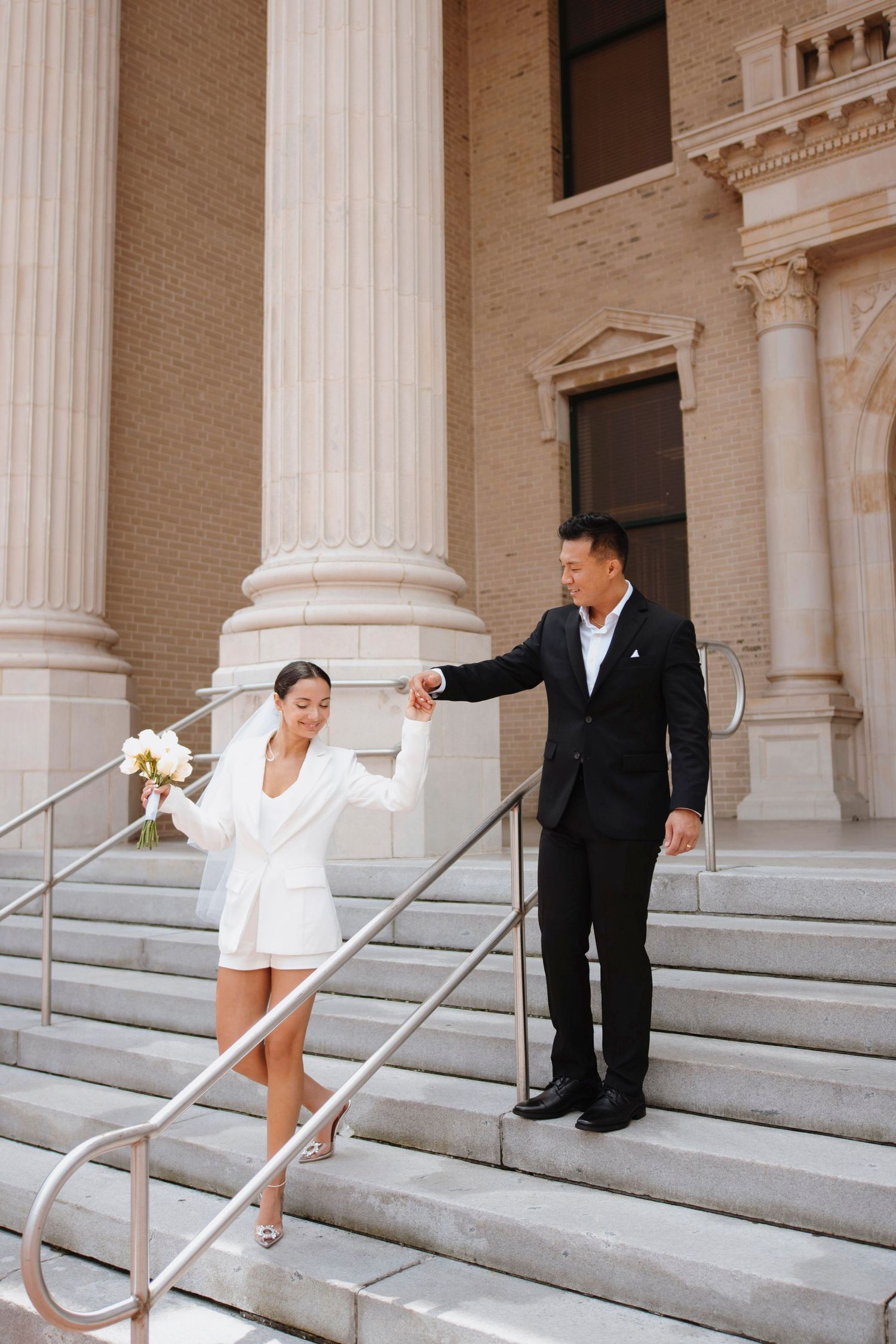 Elegant couple on courthouse steps with bride in white dress and groom in black suit.
