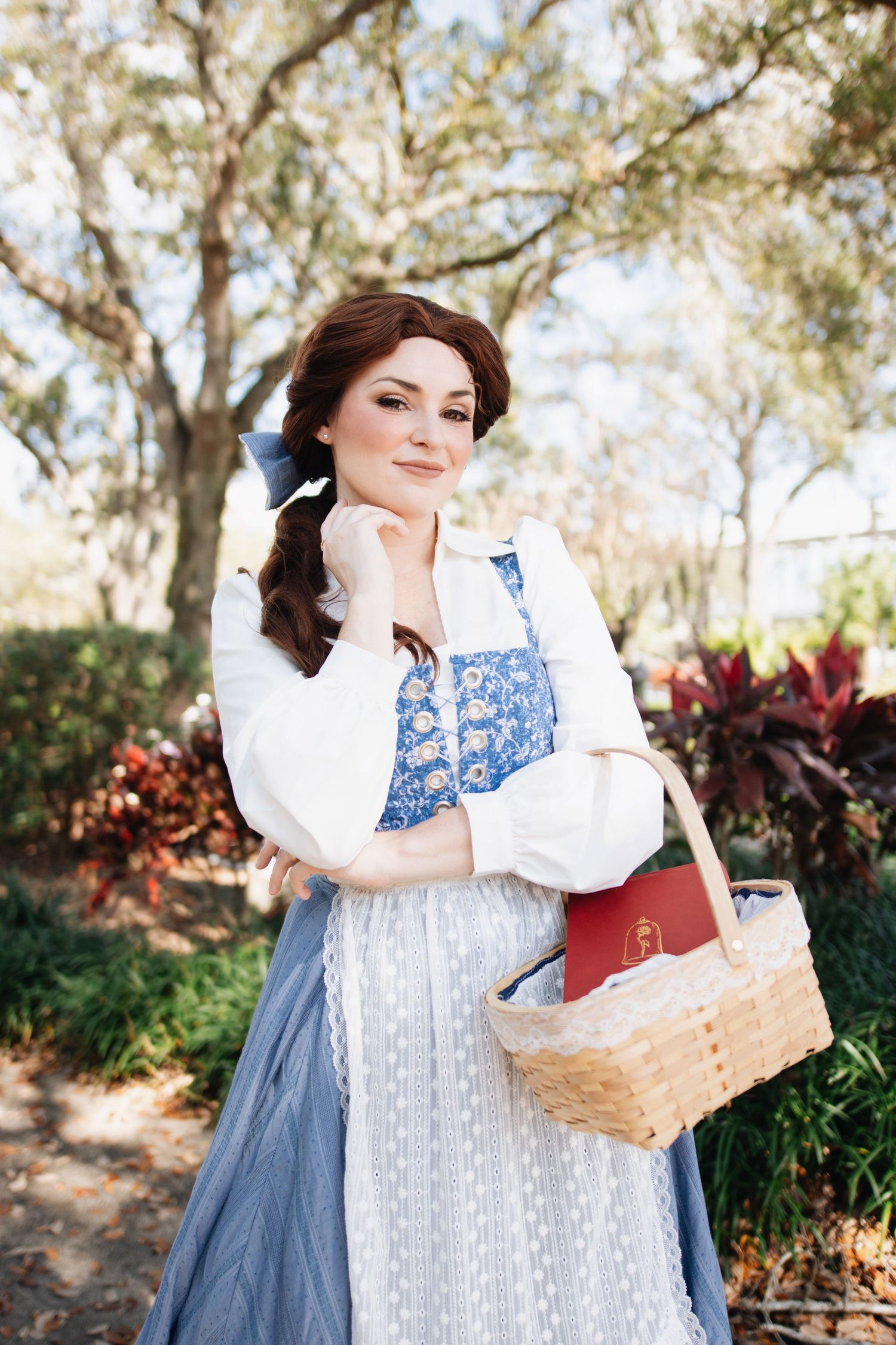 Person in blue and white vintage dress poses with wicker basket in garden setting.
