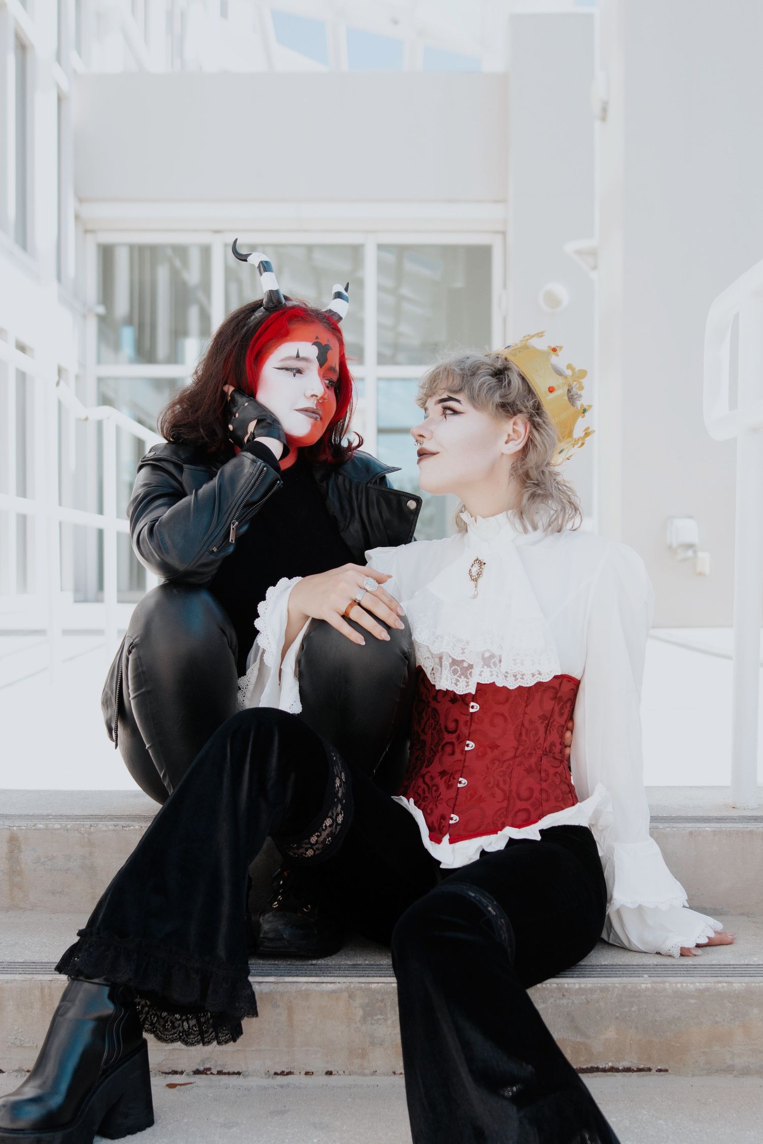 Dramatic cosplay scene with gothic-styled performers in red and white against light background.
