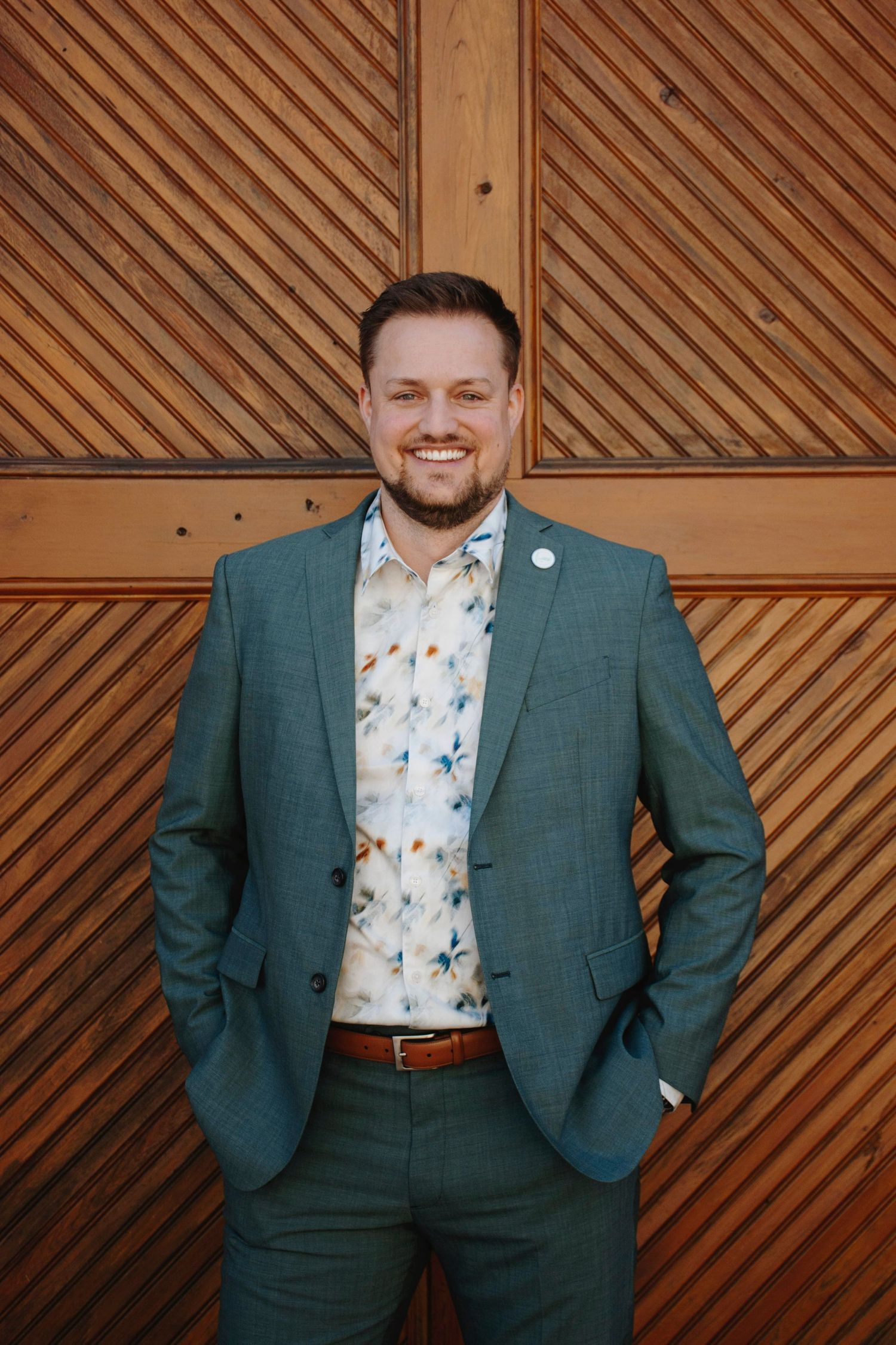 Professional portraits against wooden diagonal pattern wall wearing green suit.