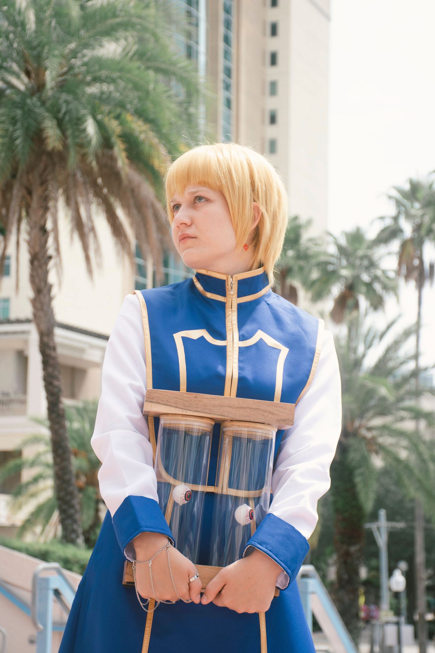 Cosplayer in blue and white uniform poses against palm tree background.