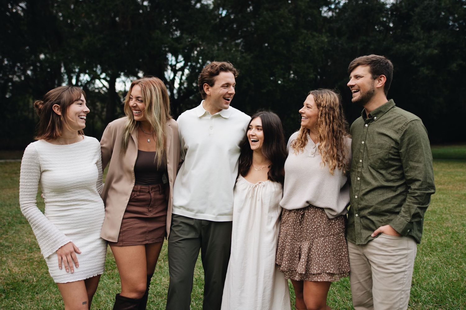 A group of people wearing neutral colored outfits stand together outdoors in a casual gathering formation.