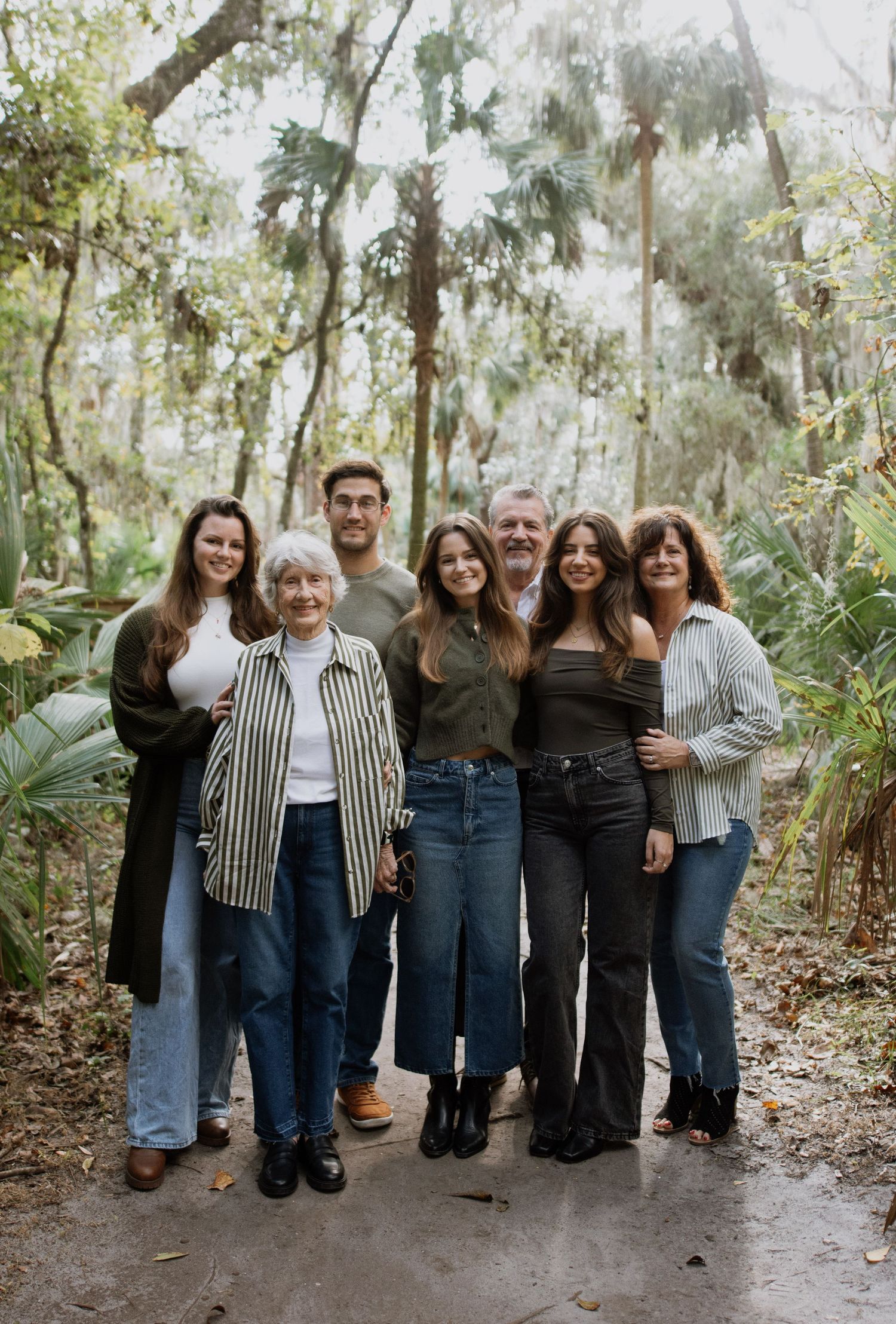 A group of people wearing coordinated denim and black outfits pose together in a lush wooded outdoor setting.