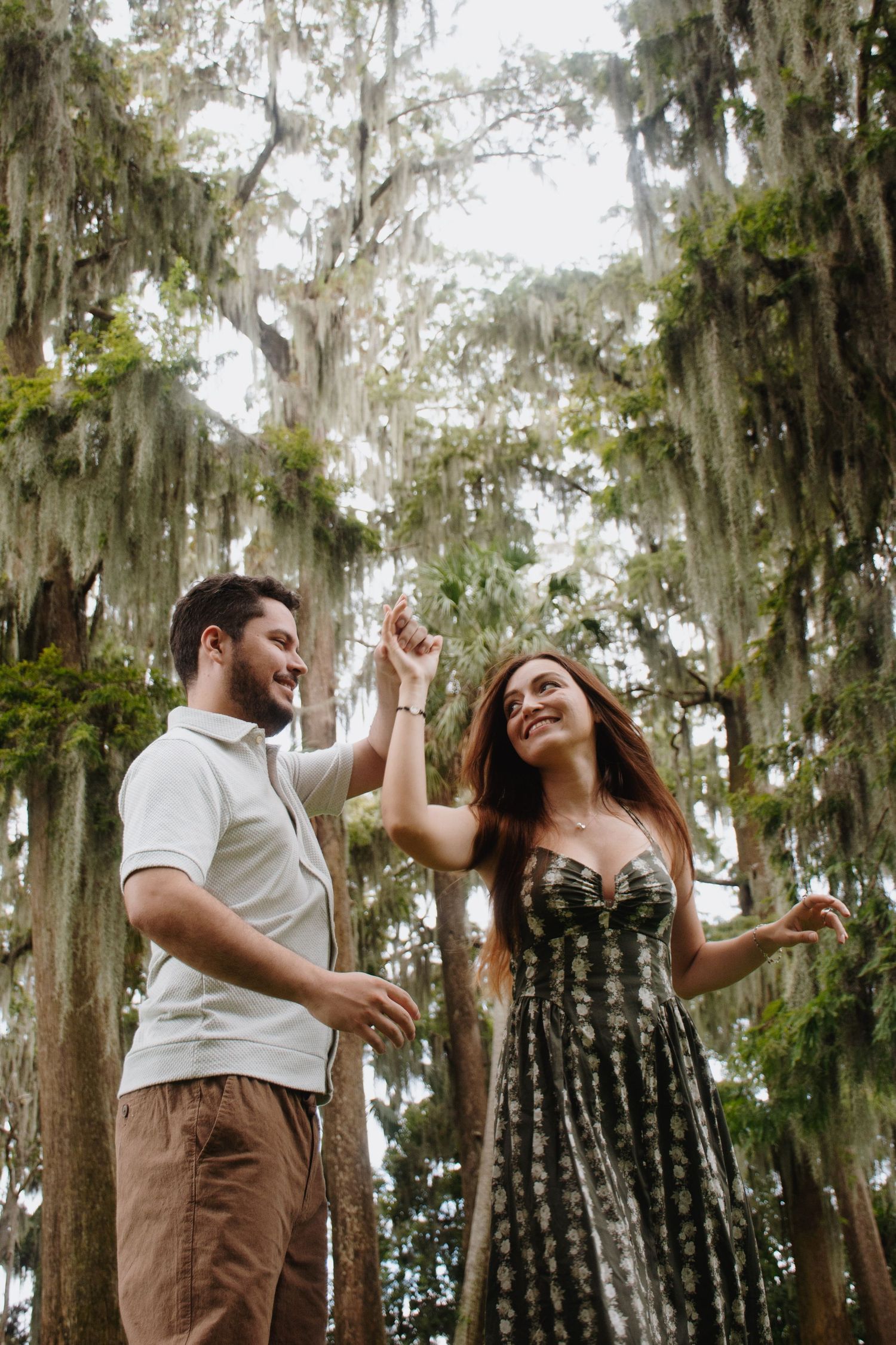 A couple dances together under Spanish moss hanging from trees in a romantic outdoor setting.
