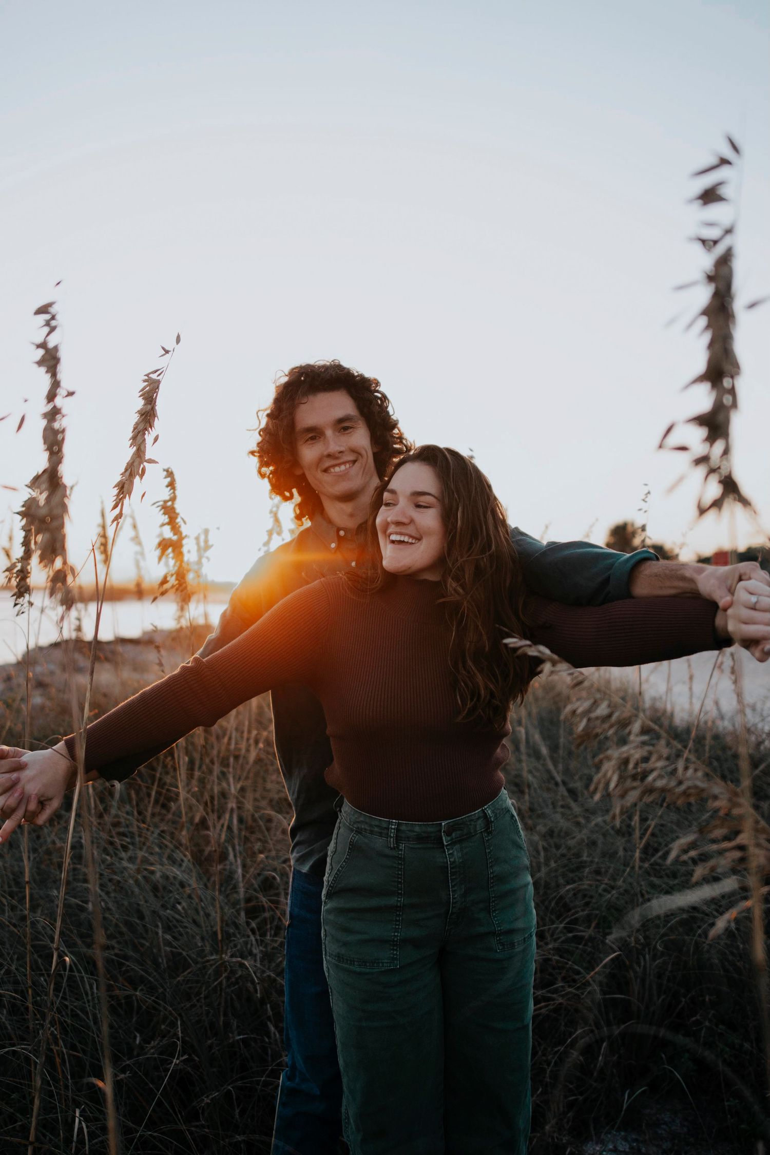 A couple embraces in a field of tall grass during golden hour sunset.